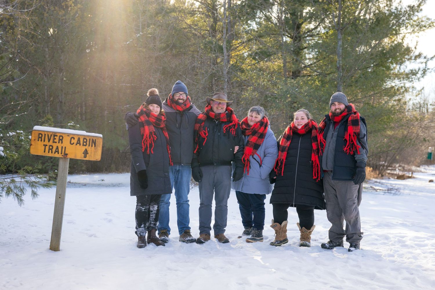 A group wearing winter coats and hats stands in a snowy landscape near a trail sign. Ottawa Family Photographer