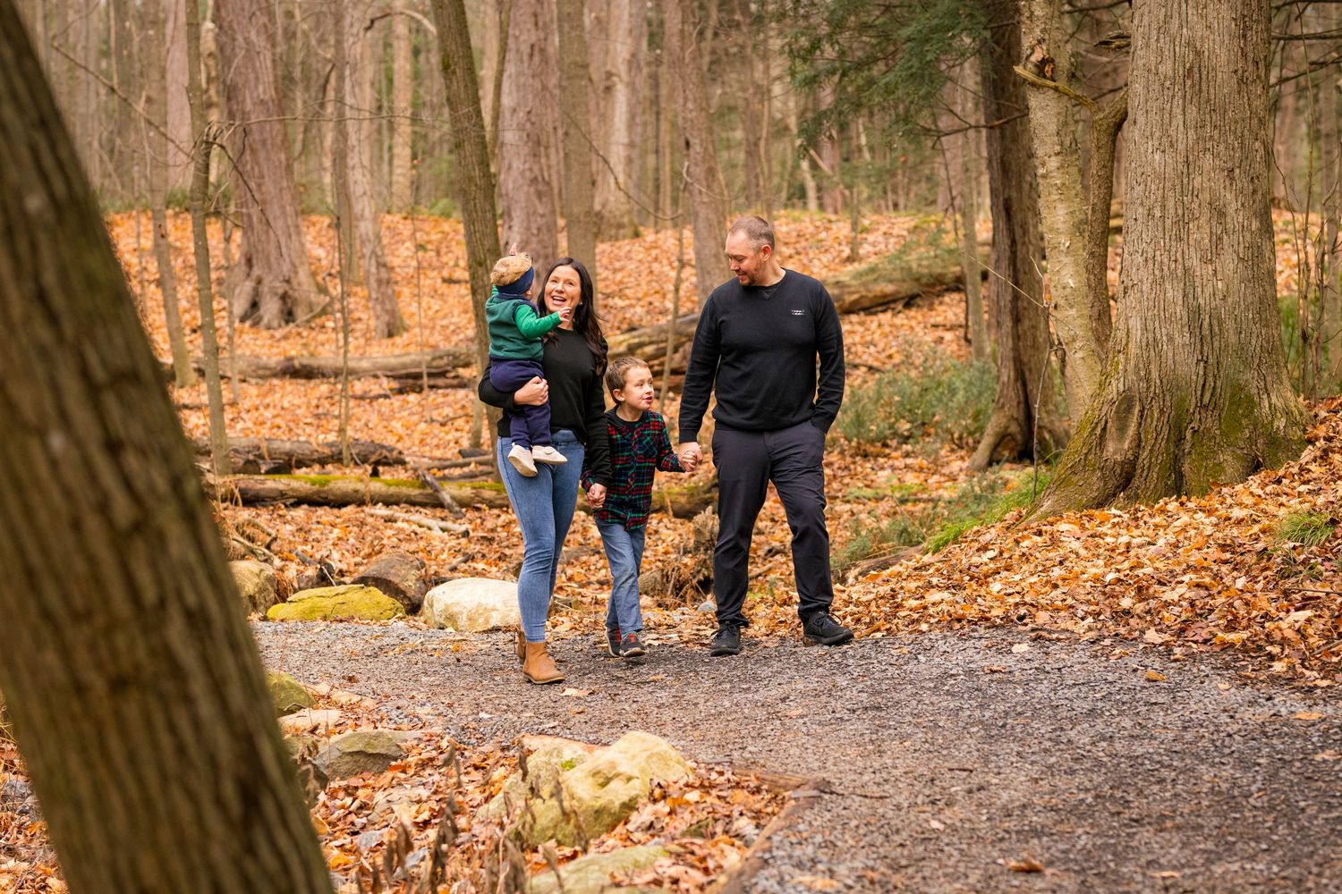 People walk together on an autumn trail covered in fallen leaves through a peaceful wooded forest.