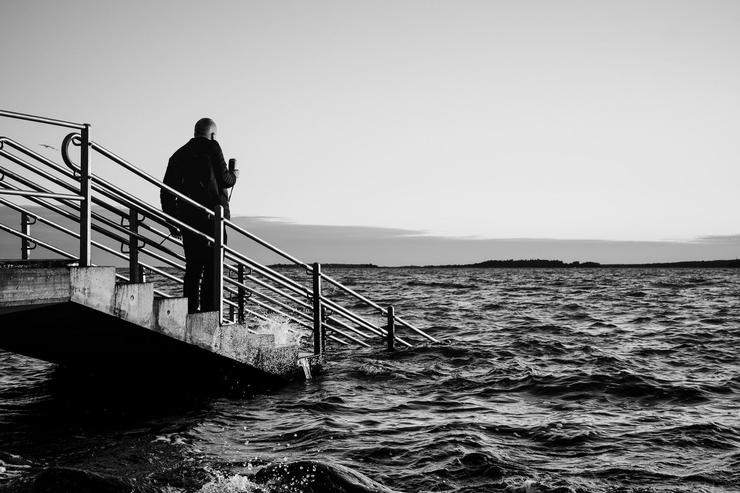 Mustavalkokuva merenranta. Lauttasaari mies rappusilla