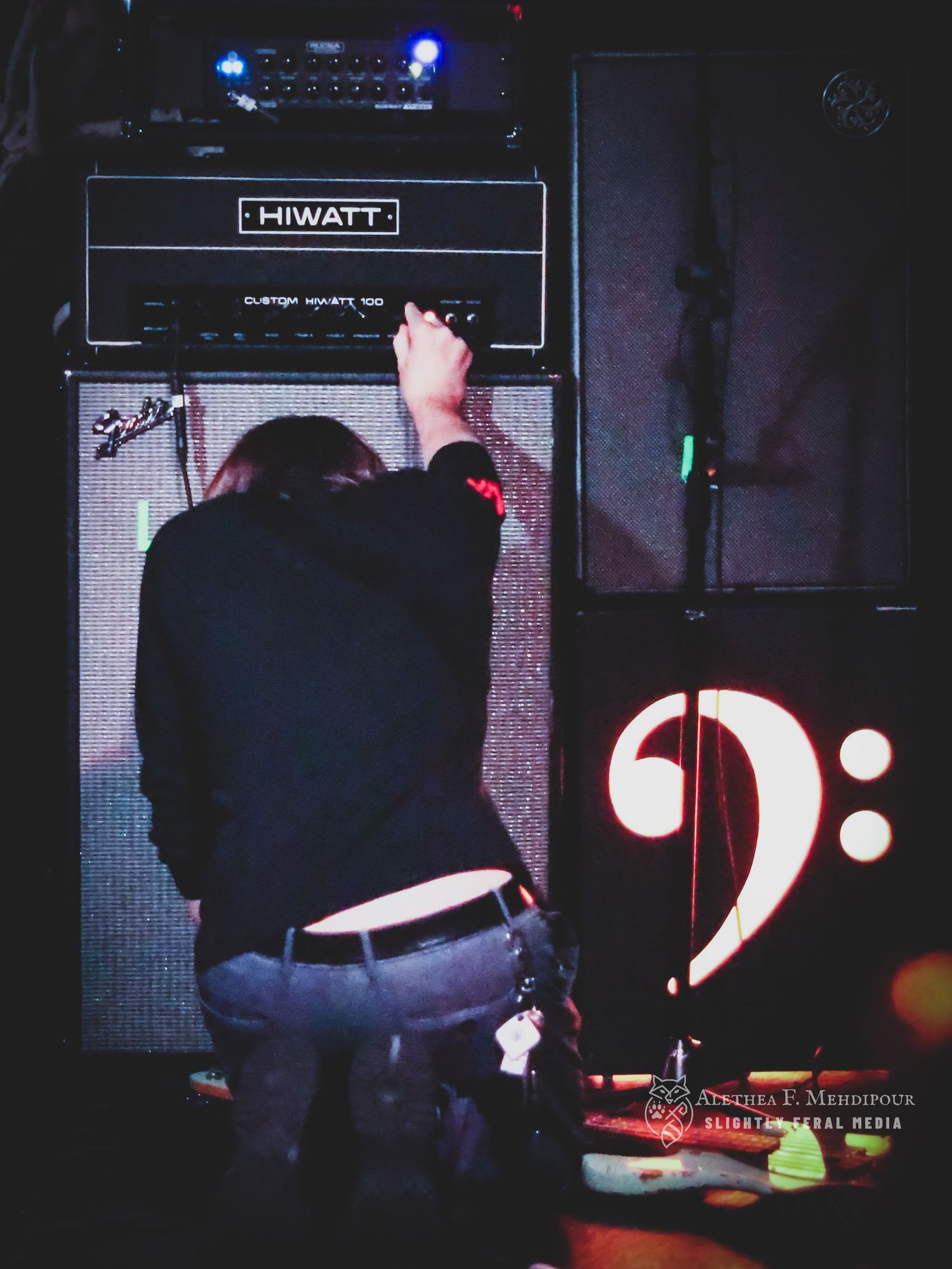Man kneeling beside amp with bass clef sign.