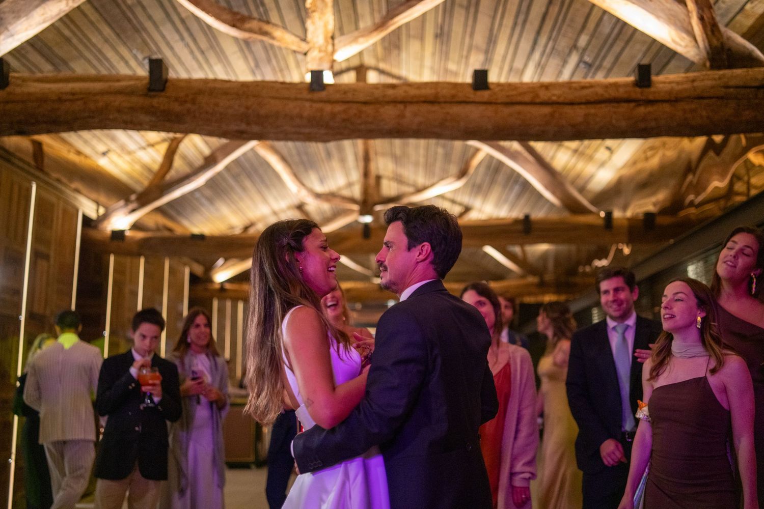 Primeira dança dos noivos durante festa de casamento, momento emotivo com iluminação quente e convidados em redor.