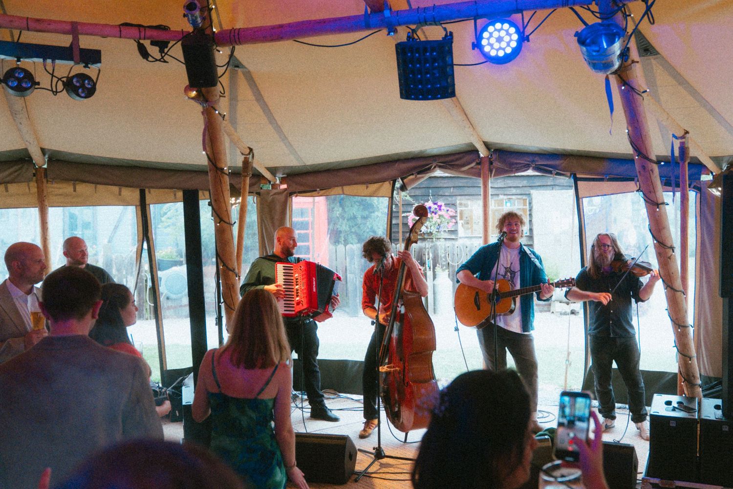Live folk band performing with accordion and double bass inside a wedding tent.