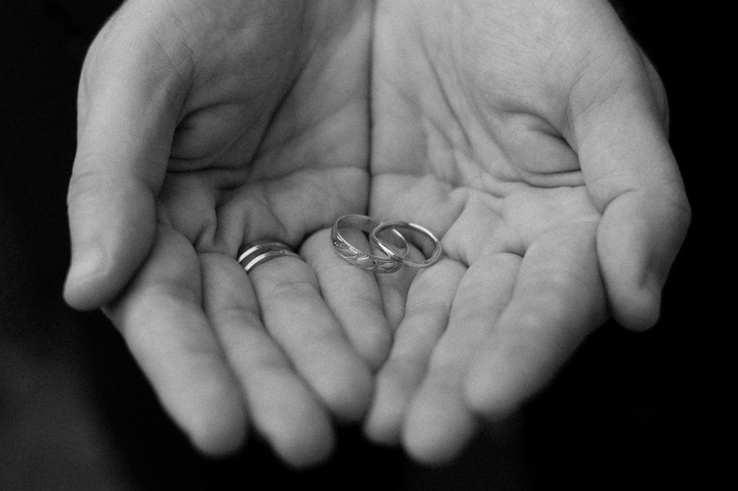 Black and white photo of two open hands cradling a pair of wedding rings, symbolizing love, commitment, and marriage.