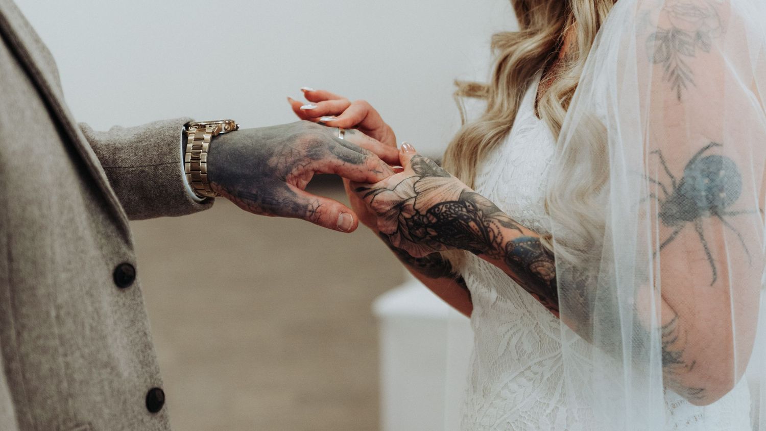 Close-up of tattooed hands exchanging wedding rings during intimate wedding ceremony.