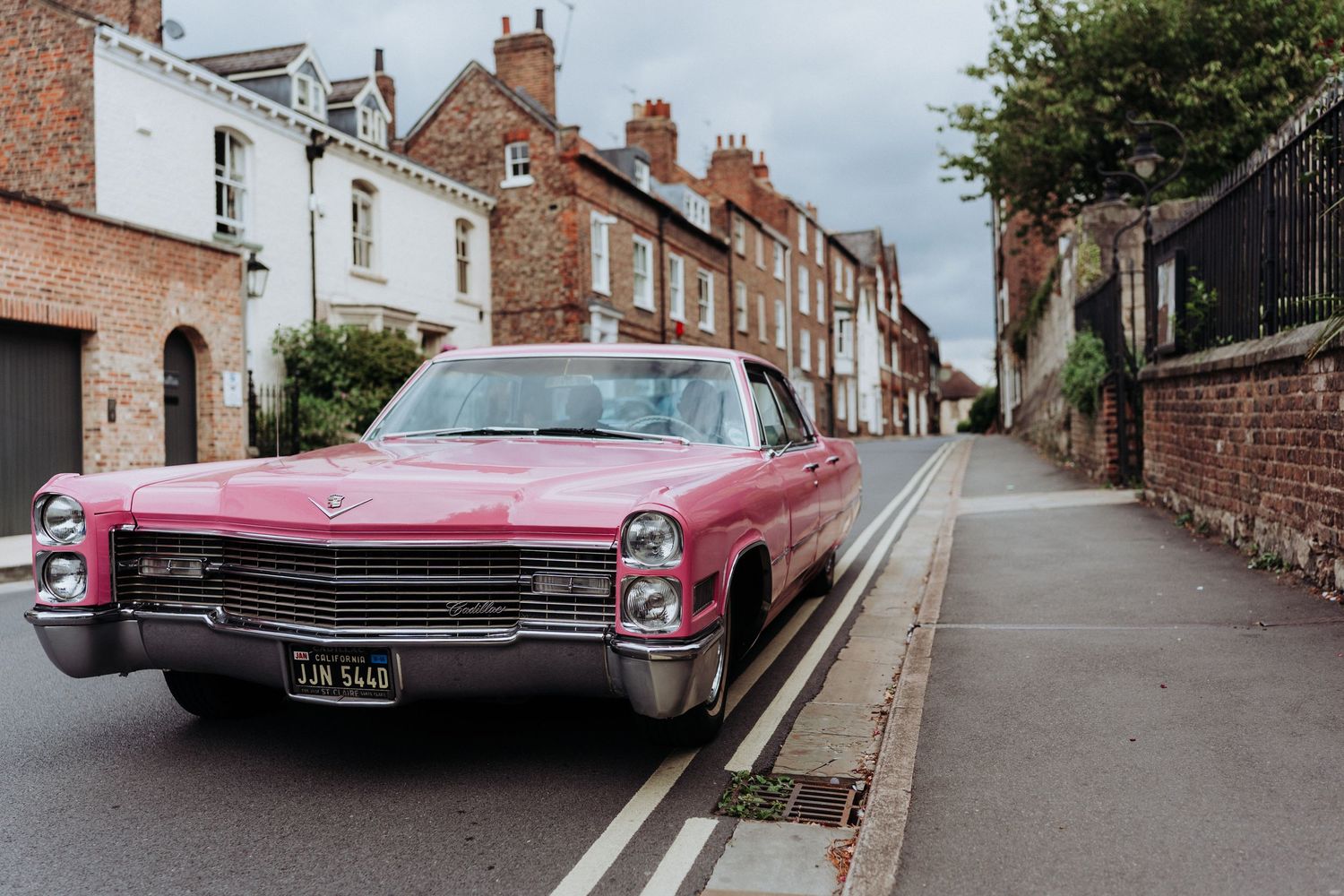 Vintage pink Cadillac parked on a quiet cobblestone street lined with brick buildings.