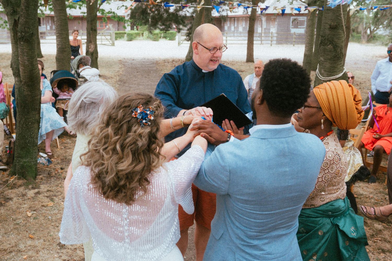 Outdoor wedding ceremony with couple holding hands before officiant under trees.
