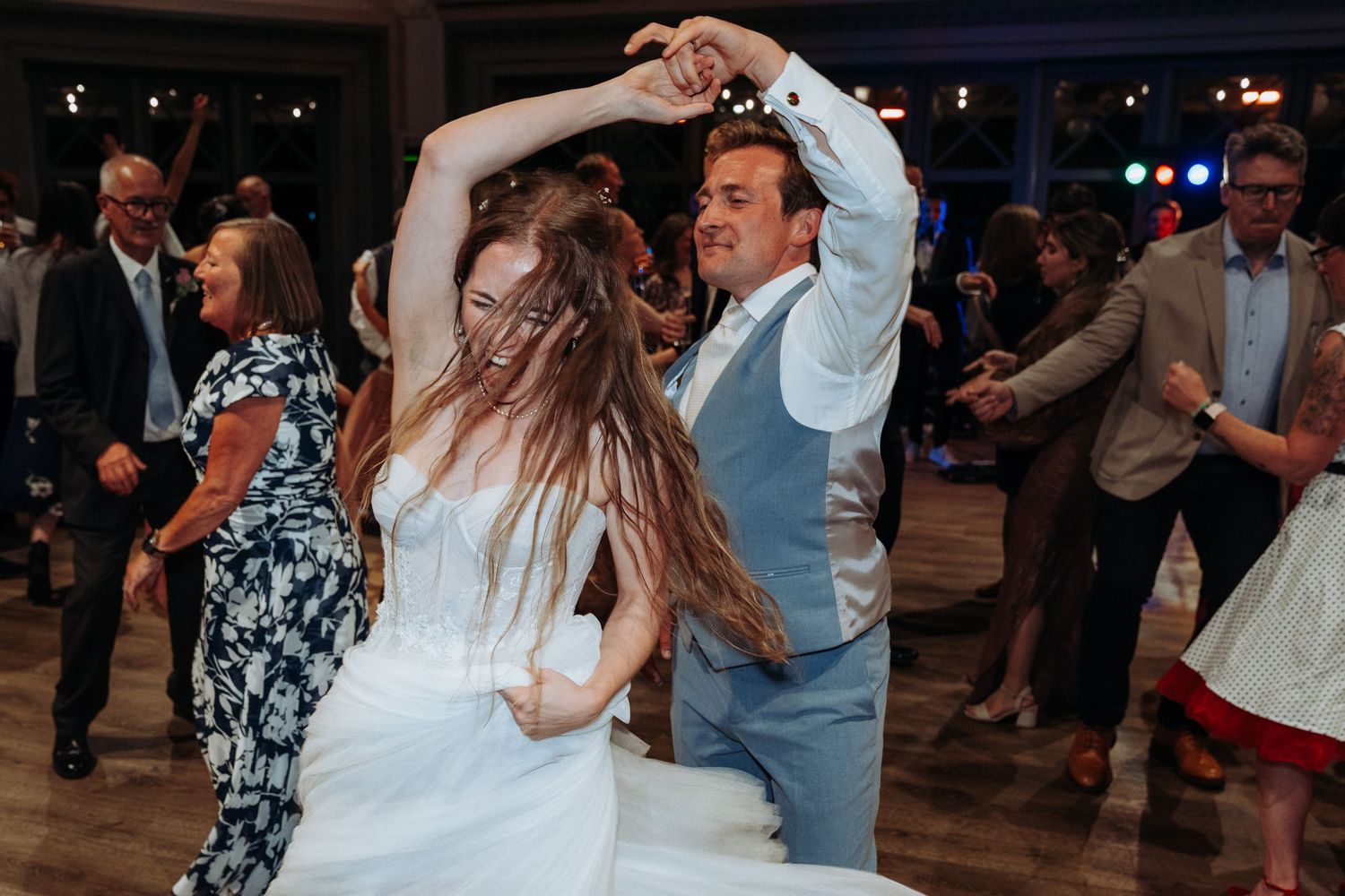 Bride and groom dancing joyfully together at their wedding reception on a crowded dance floor.