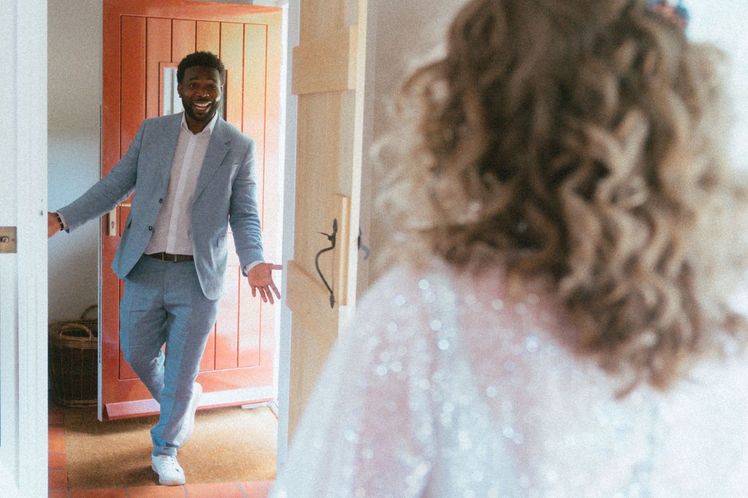 Groom in light blue suit smiling as he sees bride in white dress for the first time on wedding day.
