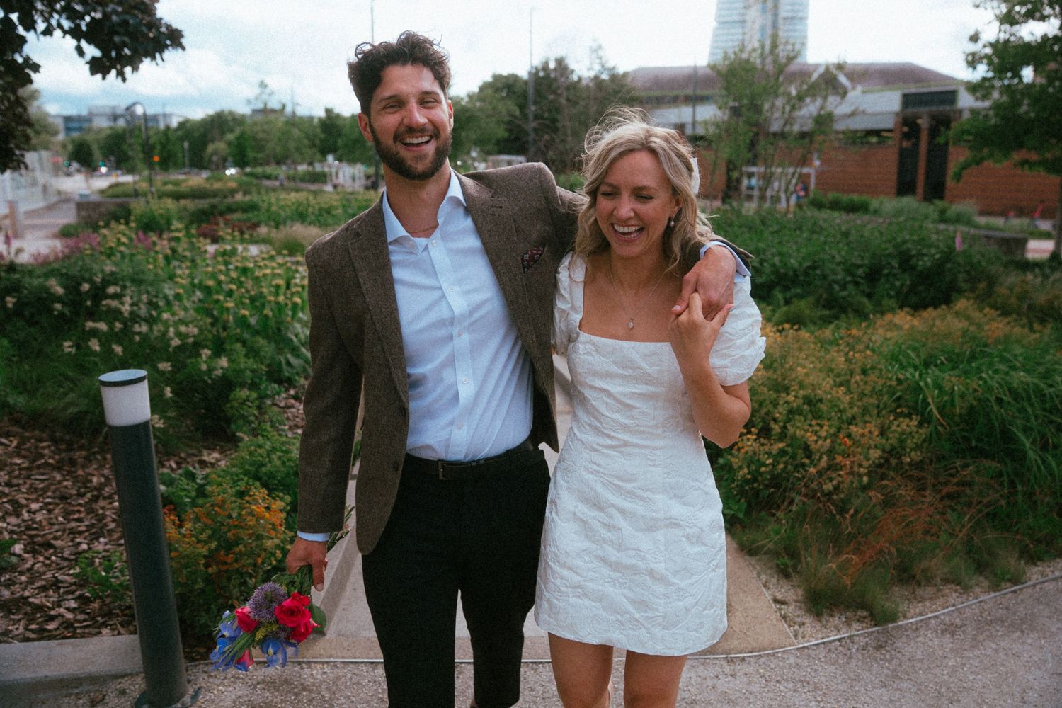 Happy couple in wedding attire smiling together outdoors in a lush garden setting.