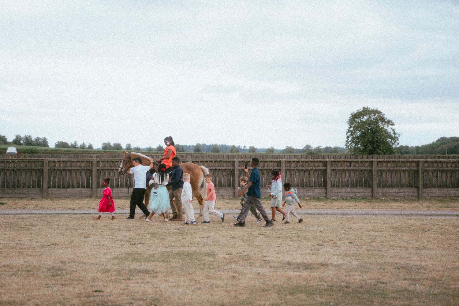 Group of adults and children walking across open field at outdoor event.