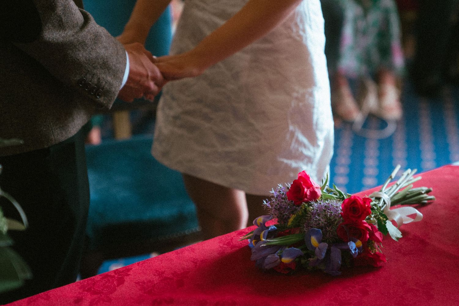 Bride and groom holding hands at altar with colorful bridal bouquet on red velvet surface.