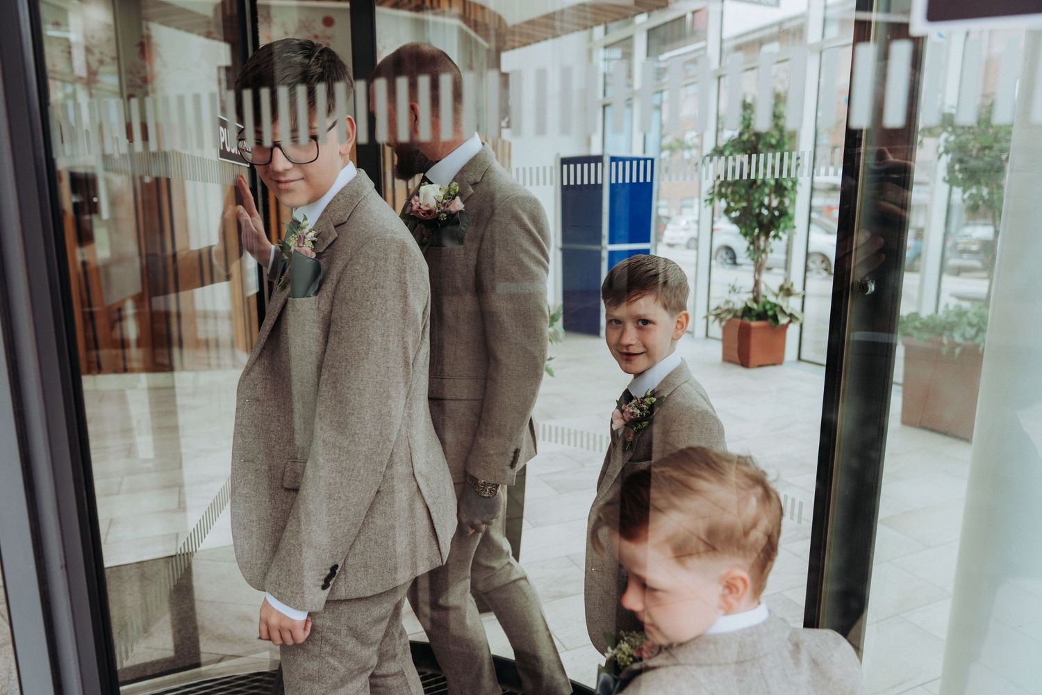 Groom and young boys in matching grey suits entering a building through revolving glass doors.
