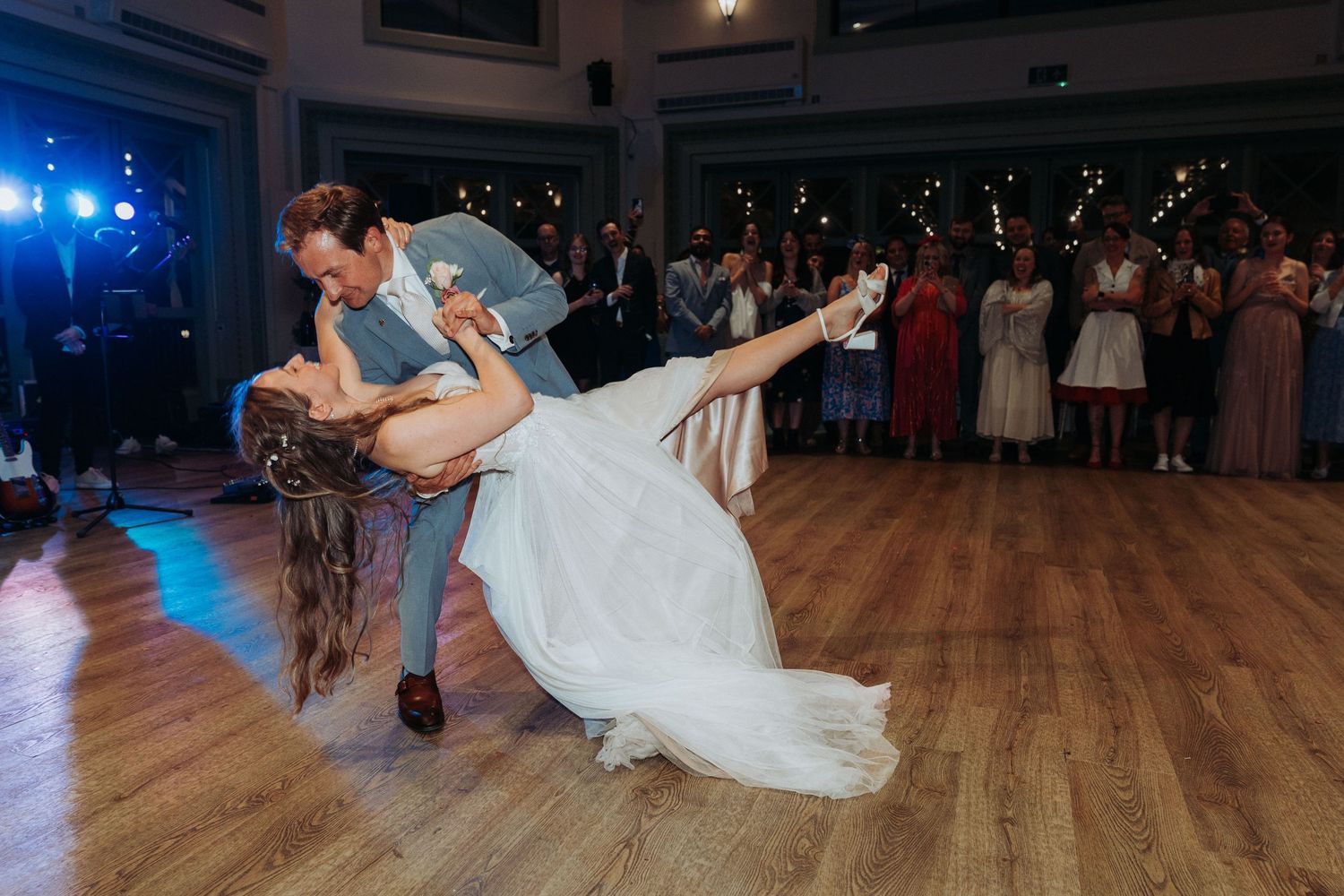 Groom dramatically dipping bride in white wedding dress during first dance at reception.