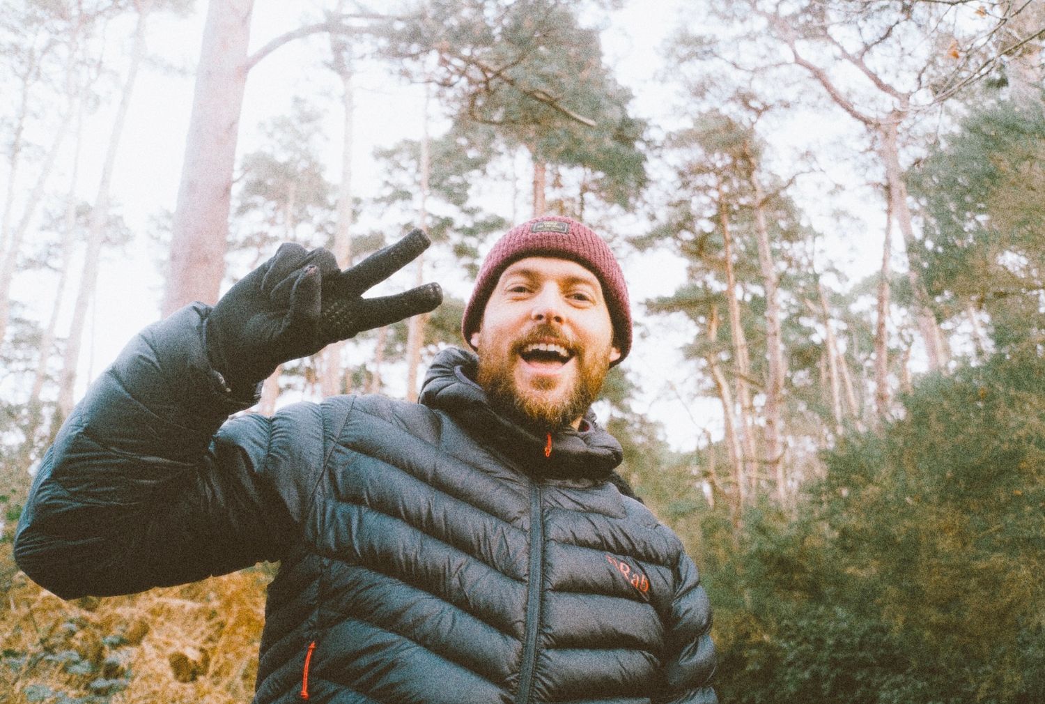 Happy bearded man making a peace sign selfie in a winter forest wearing a red beanie.