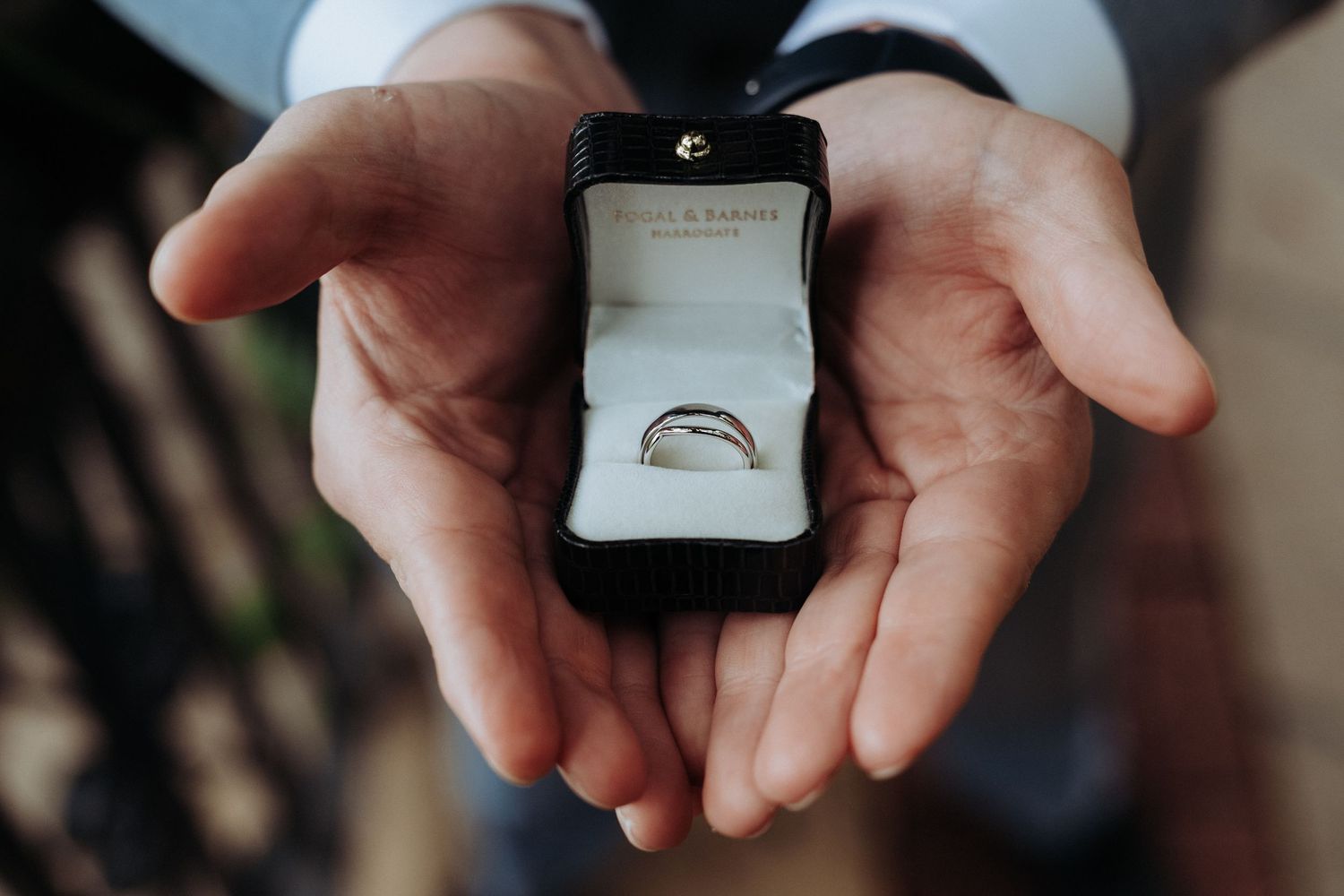 Groom holding open ring box displaying a silver wedding band before the ceremony.