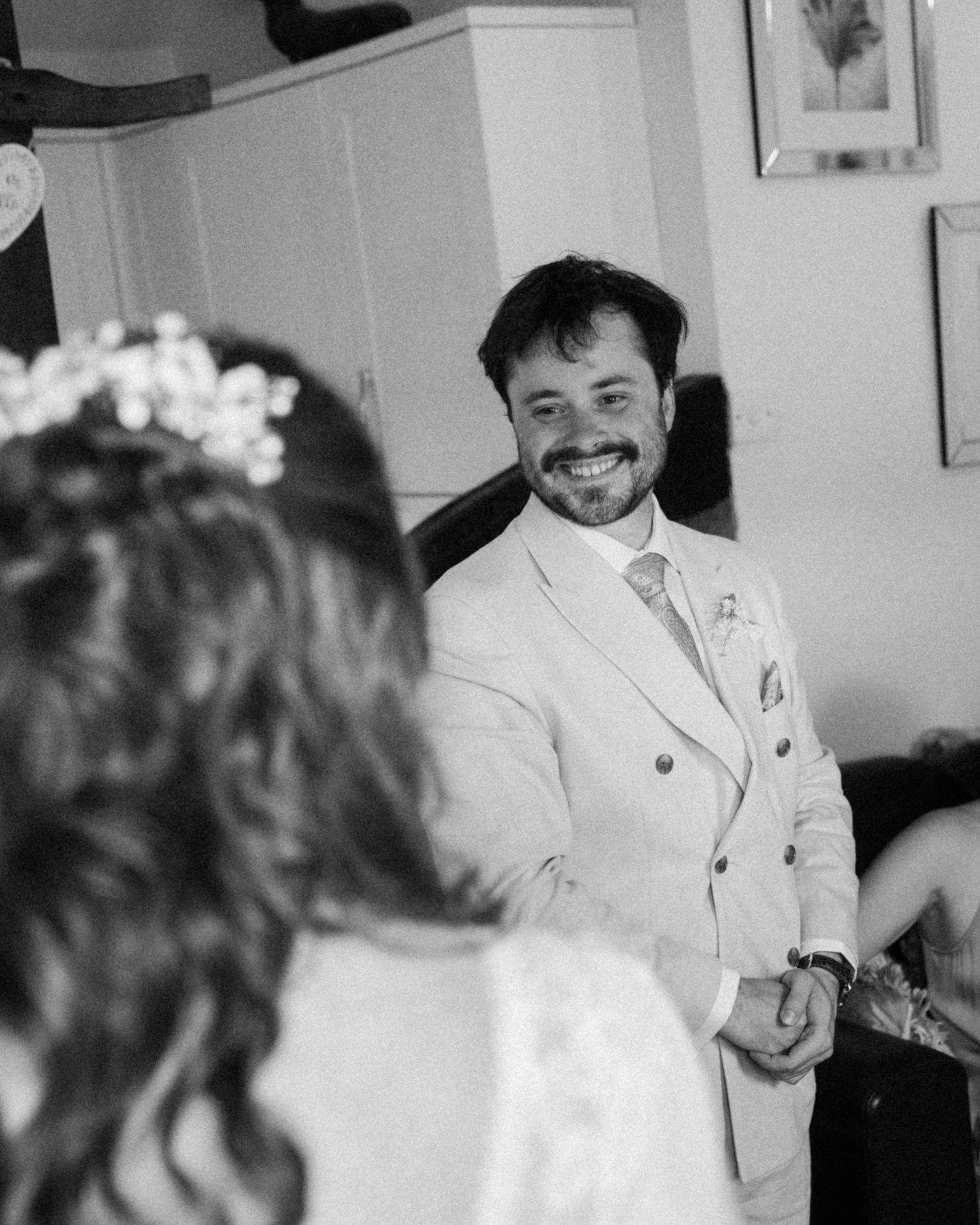 Groom in light suit smiling at bride during wedding ceremony, captured in elegant black and white photography.