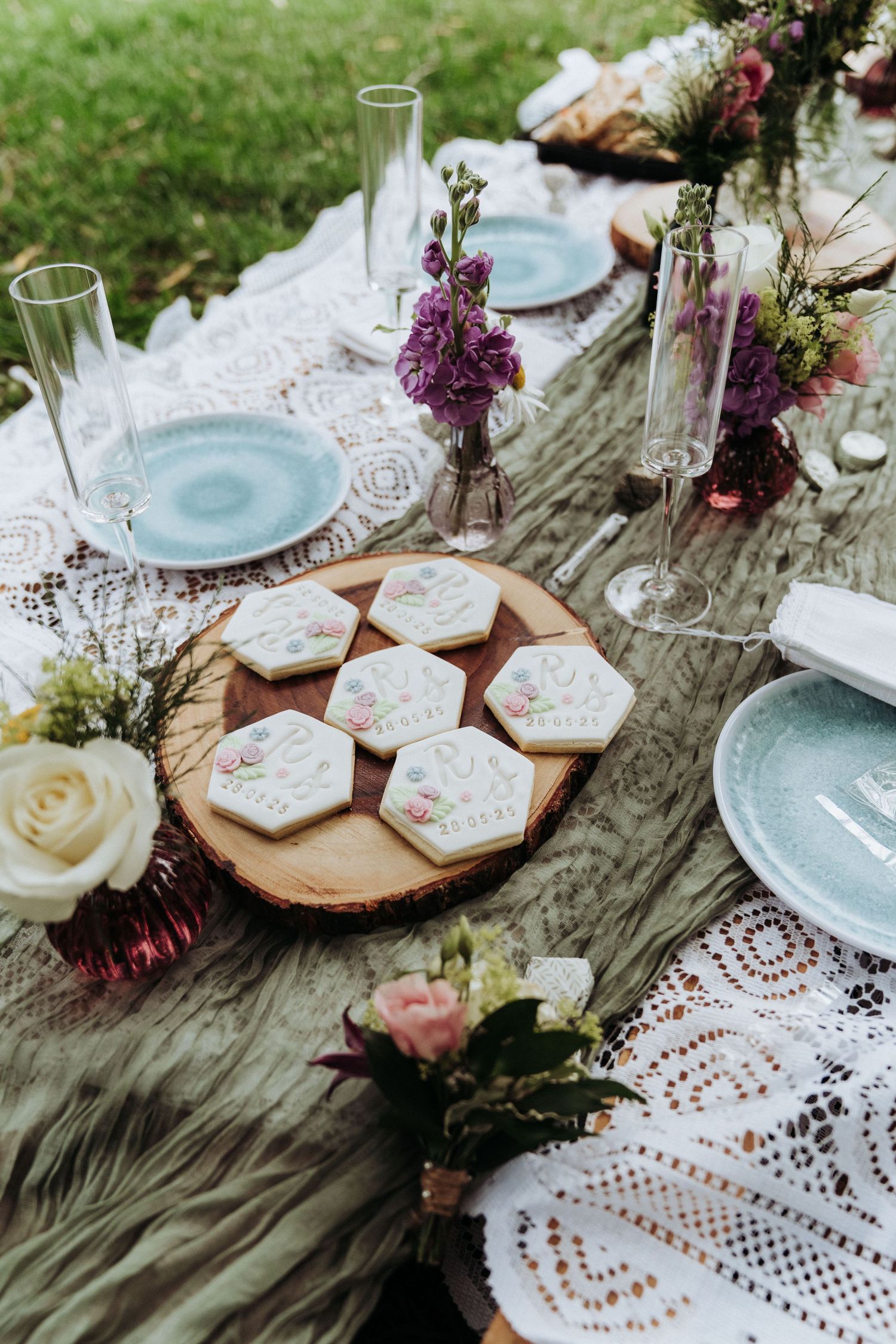 Elegant boho wedding table setting with hexagonal iced cookies on a wooden board, floral arrangements and blue plates.