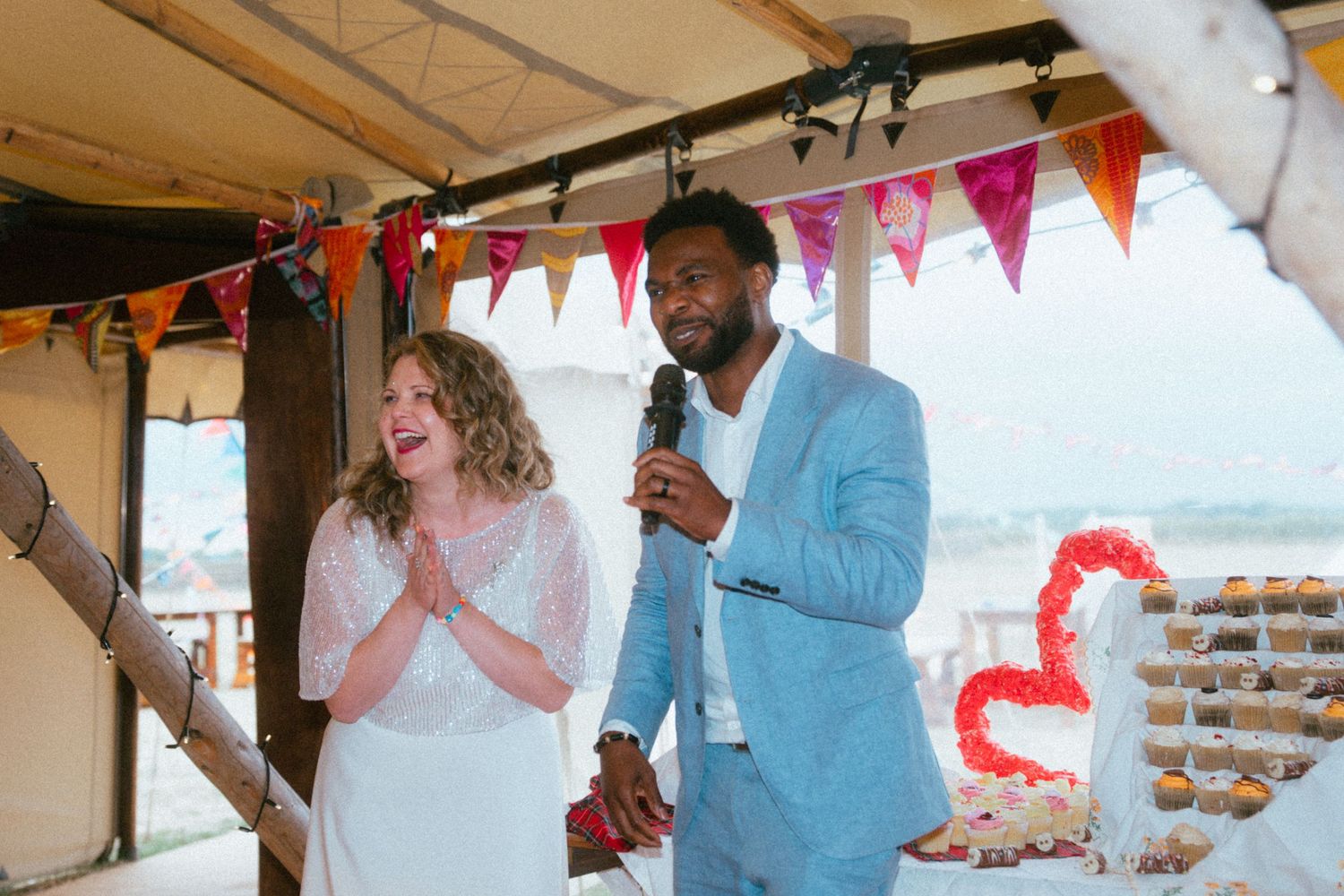 Bride and groom giving a speech under decorated tent with colorful bunting at their beach wedding reception.