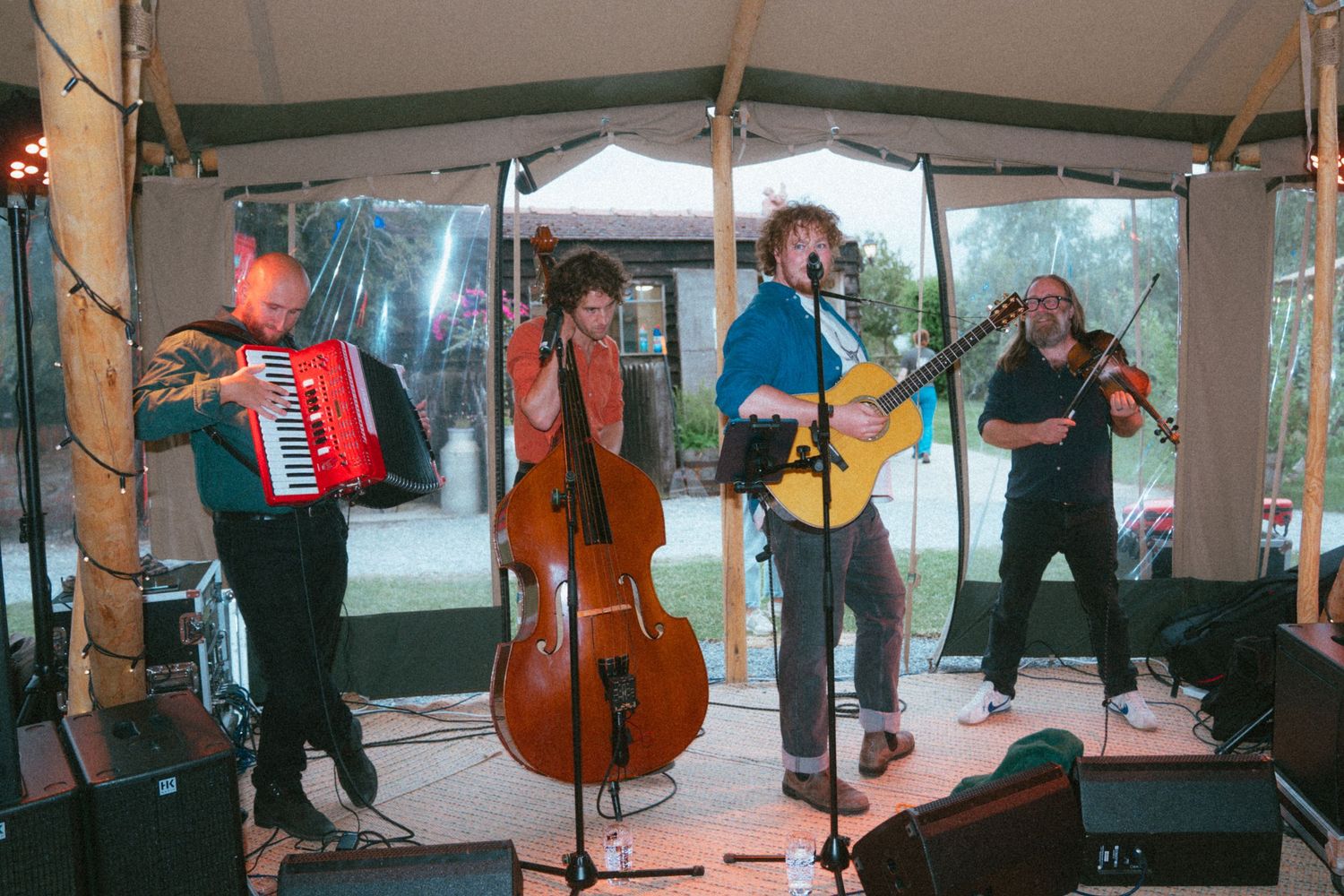 Live folk band performs with accordion, cello, guitar, and violin at an outdoor wedding reception.