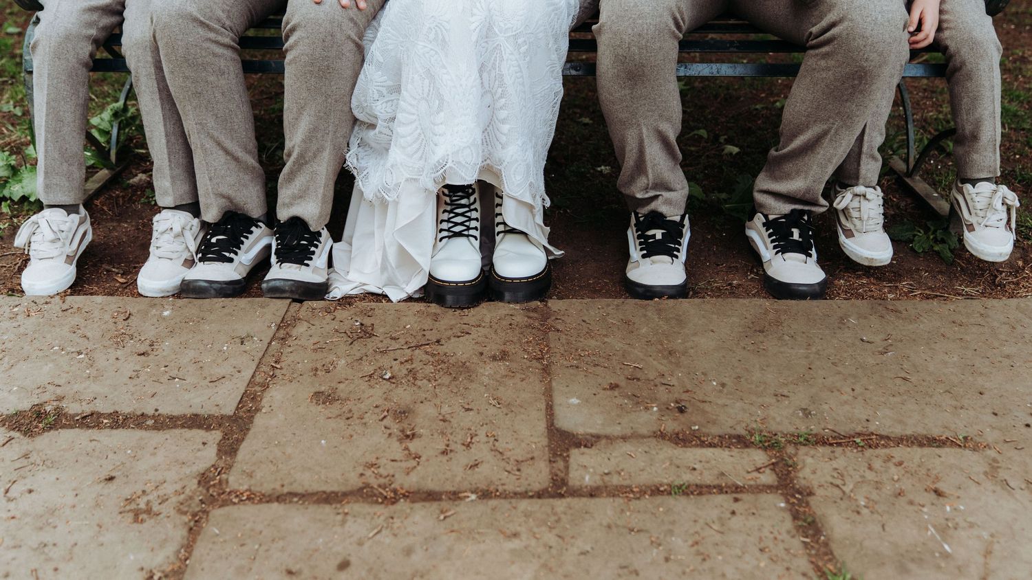 Wedding party seated on bench showing off matching white sneakers with bride in white dress.