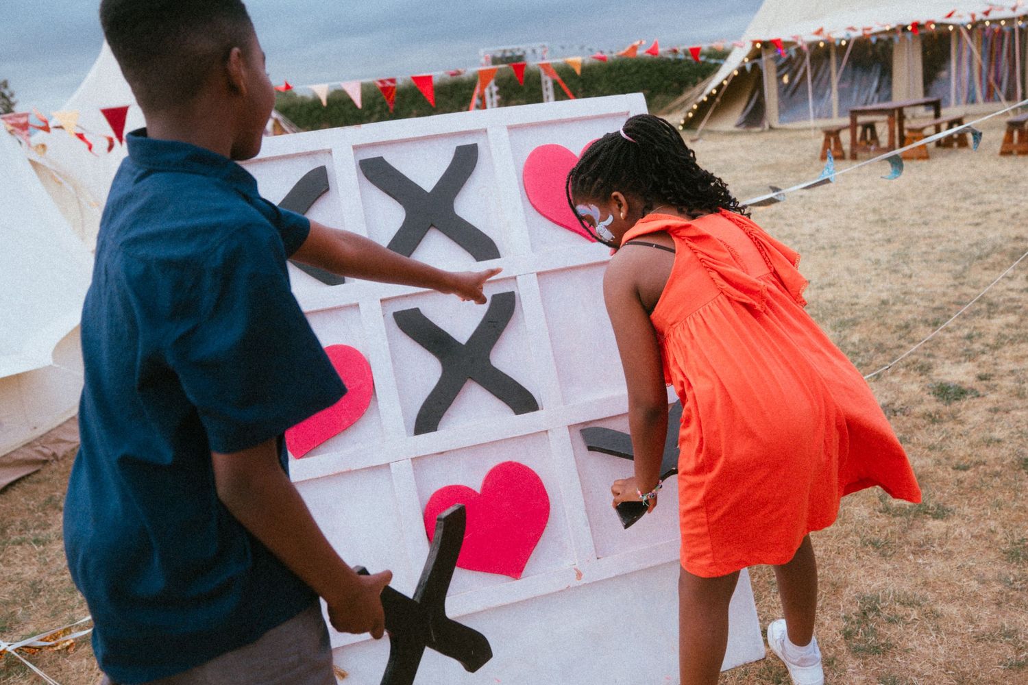 Two children play a giant tic-tac-toe game with hearts and crosses at an outdoor festival.