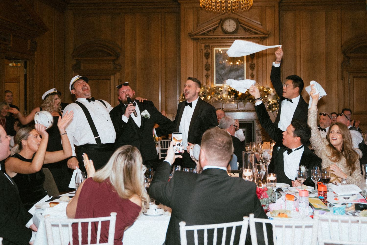 Energetic wedding reception with guests waving napkins at elegant candlelit dinner table.