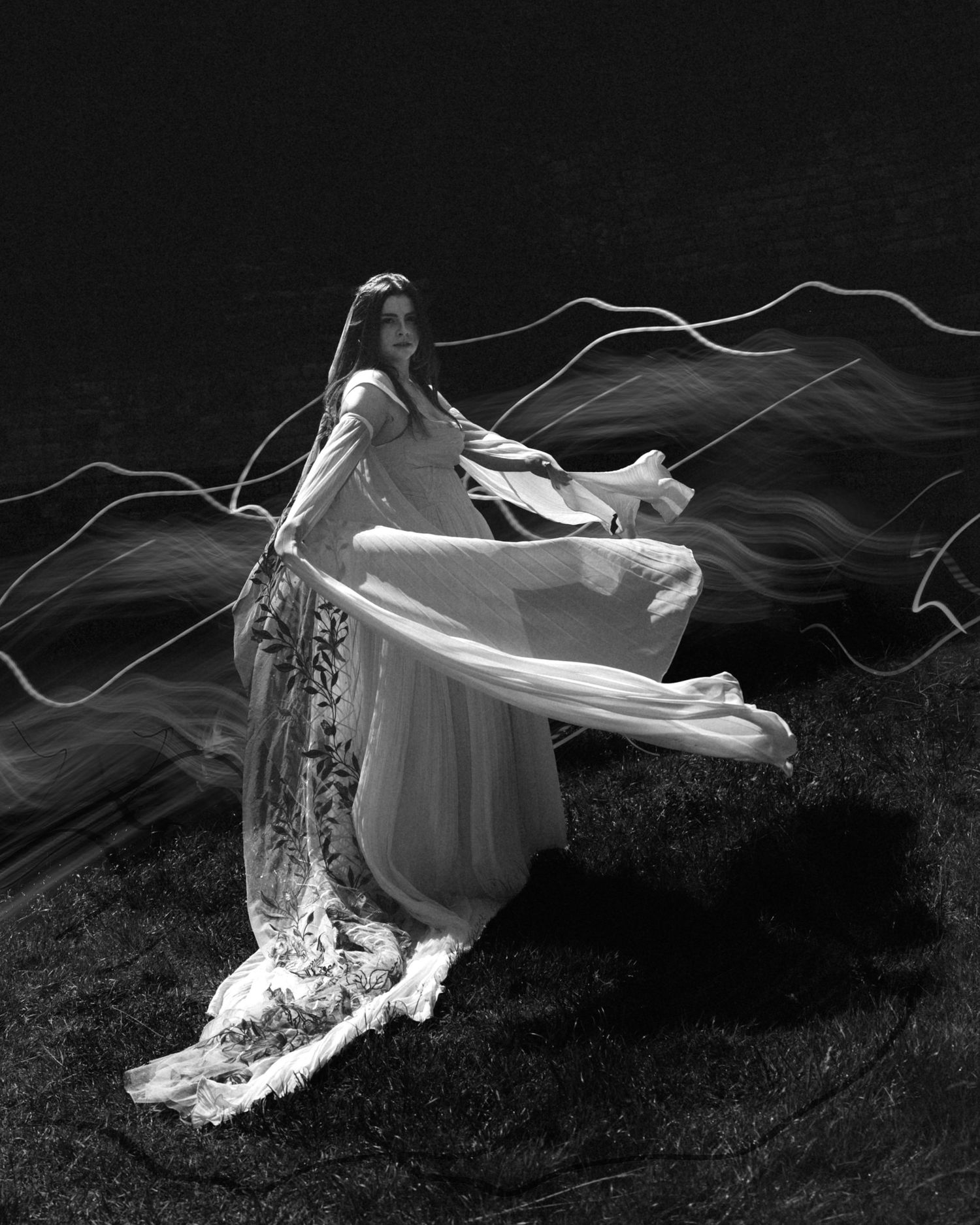 Bride in flowing white gown with veil dramatically swirling in black and white photo.