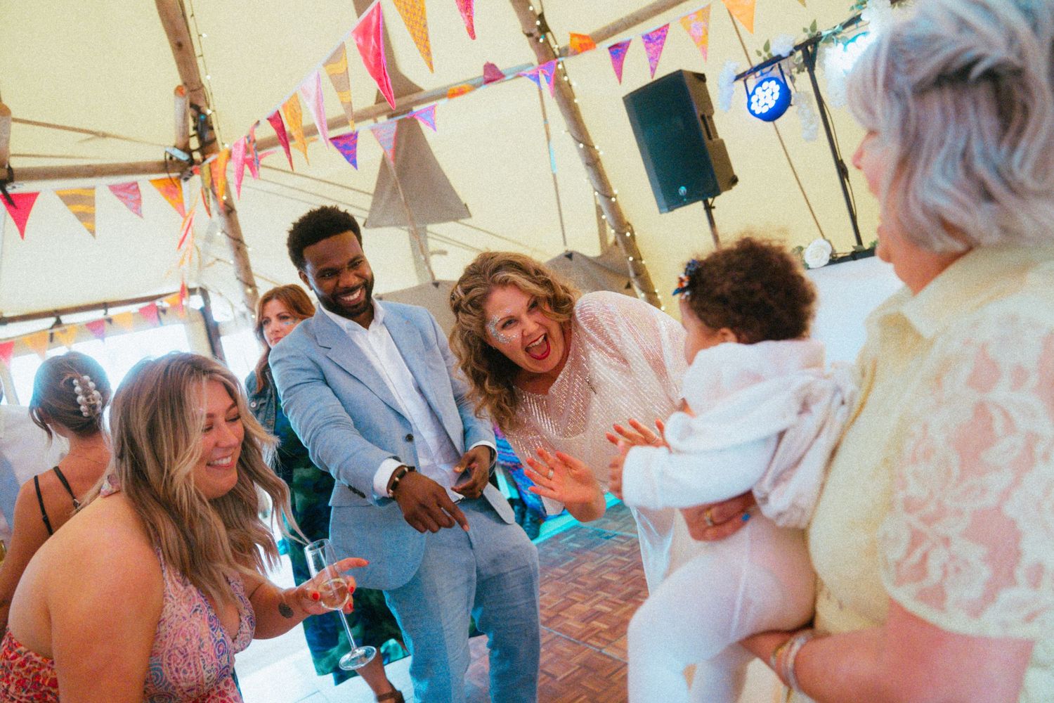 Bride and groom in tipi wedding venue smile while interacting with guests holding a baby at their reception.
