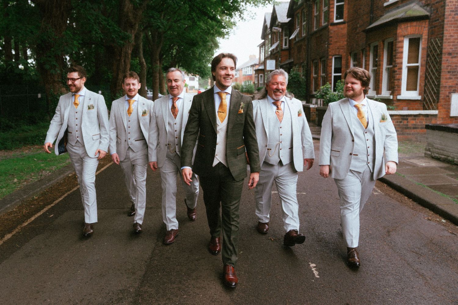 Groom and groomsmen in light grey suits walking confidently down a street on a wedding day.