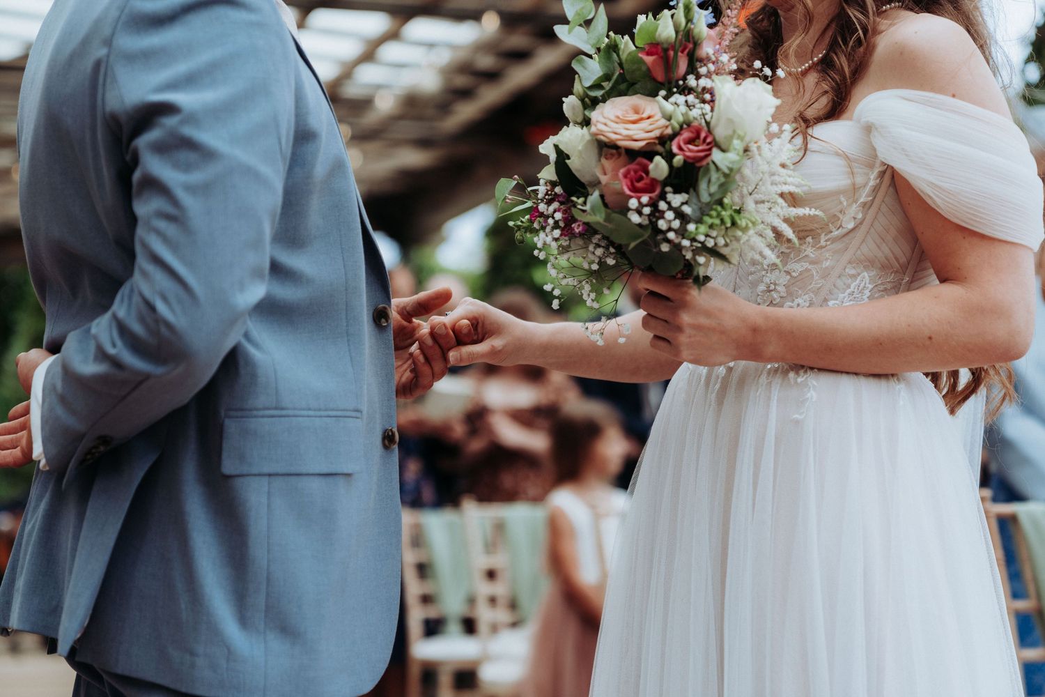 Bride and groom exchanging rings during outdoor wedding ceremony, bride holding colorful floral bouquet.