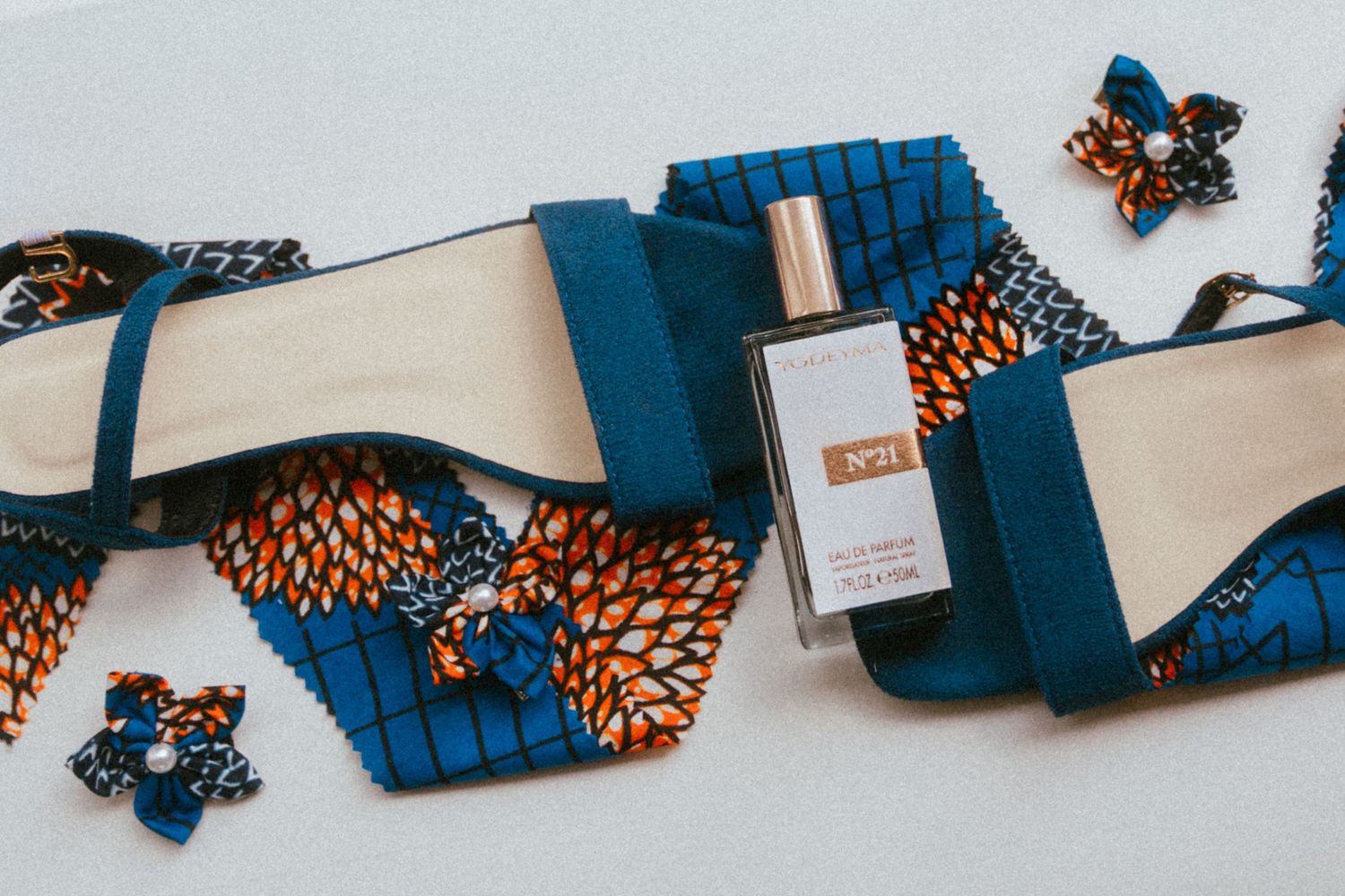 Blue African print sandals with matching floral accessories and a No.1 perfume bottle on white background.
