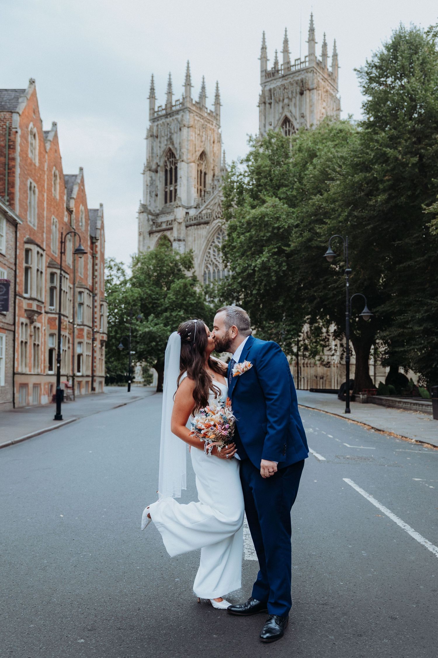 Bride and groom share a romantic kiss on an empty road with York Minster cathedral in the background.