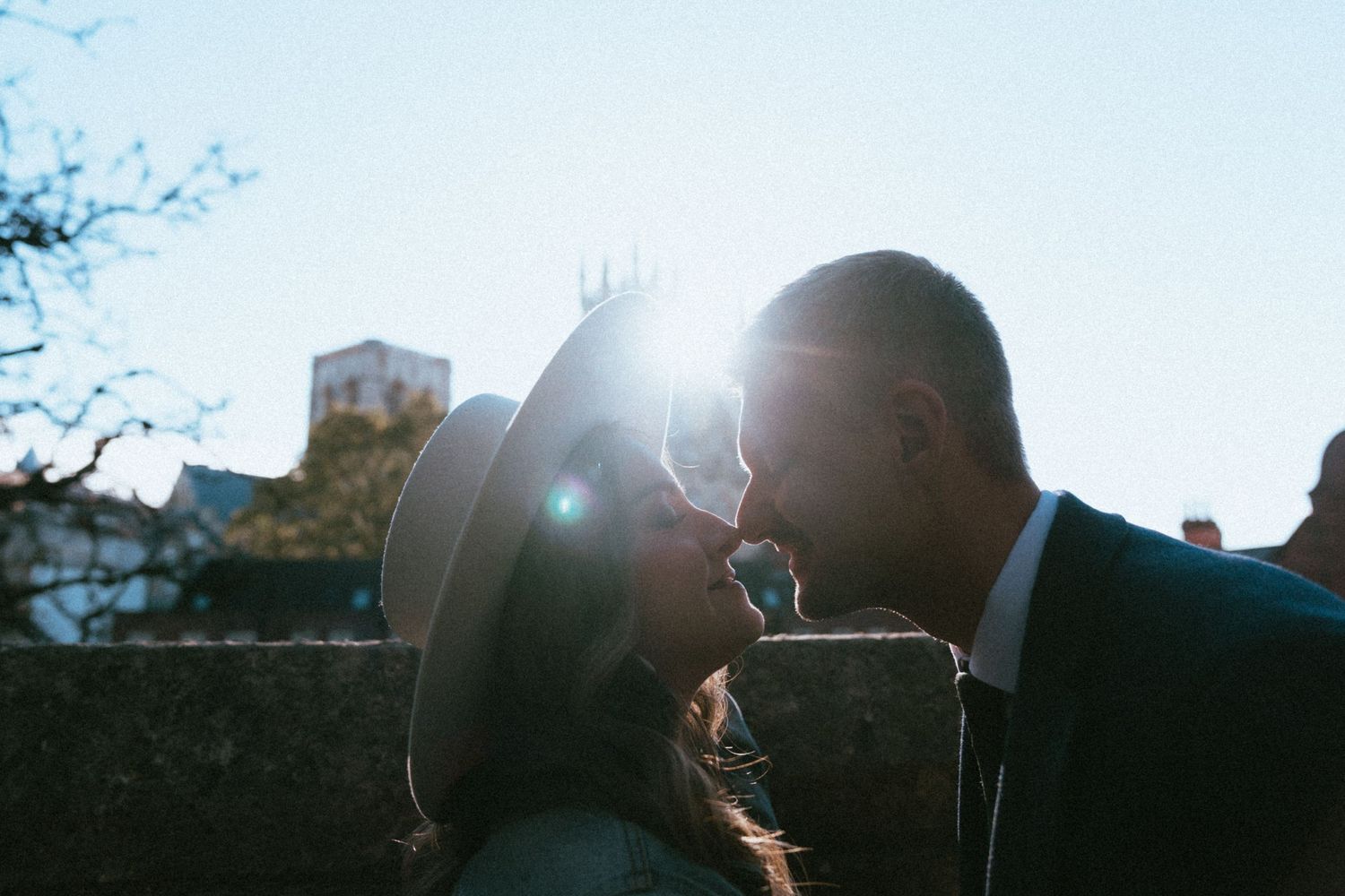 Couple sharing a romantic moment with sun flare and blue sky behind a historic building.