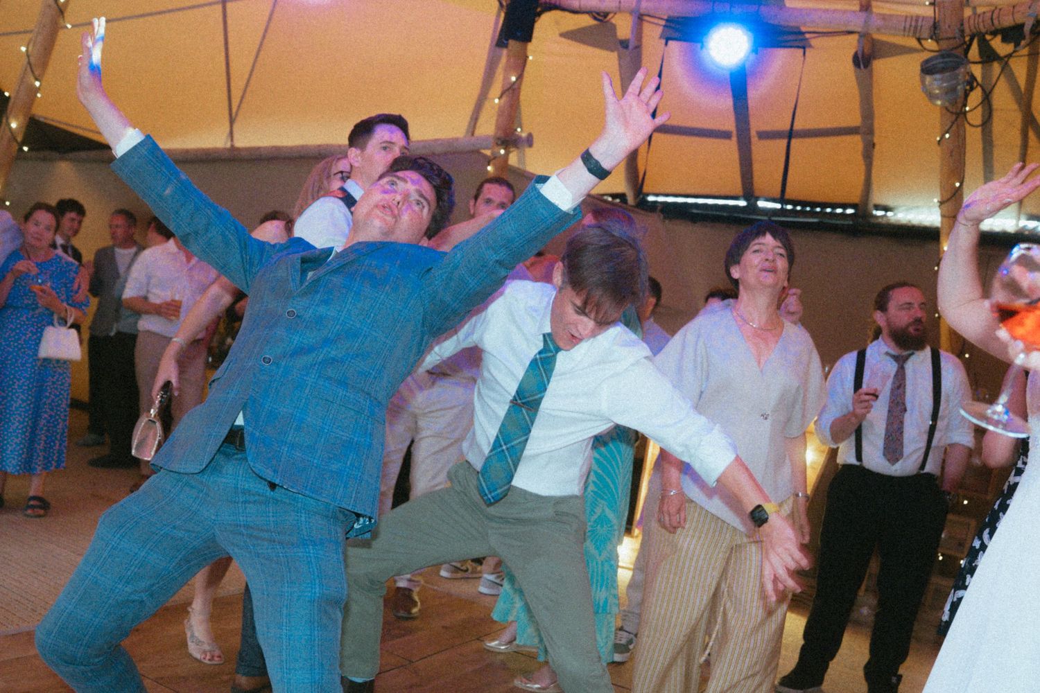 Energetic wedding guests dancing enthusiastically on the dance floor at evening reception.