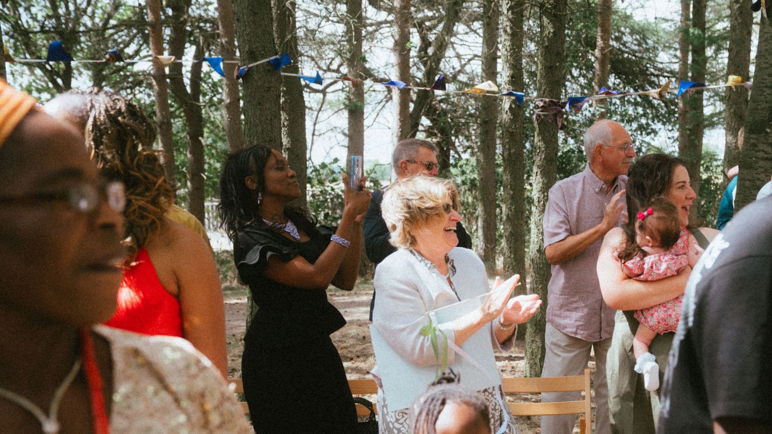 Guests clapping and celebrating at an outdoor woodland wedding ceremony with colorful bunting decorations.