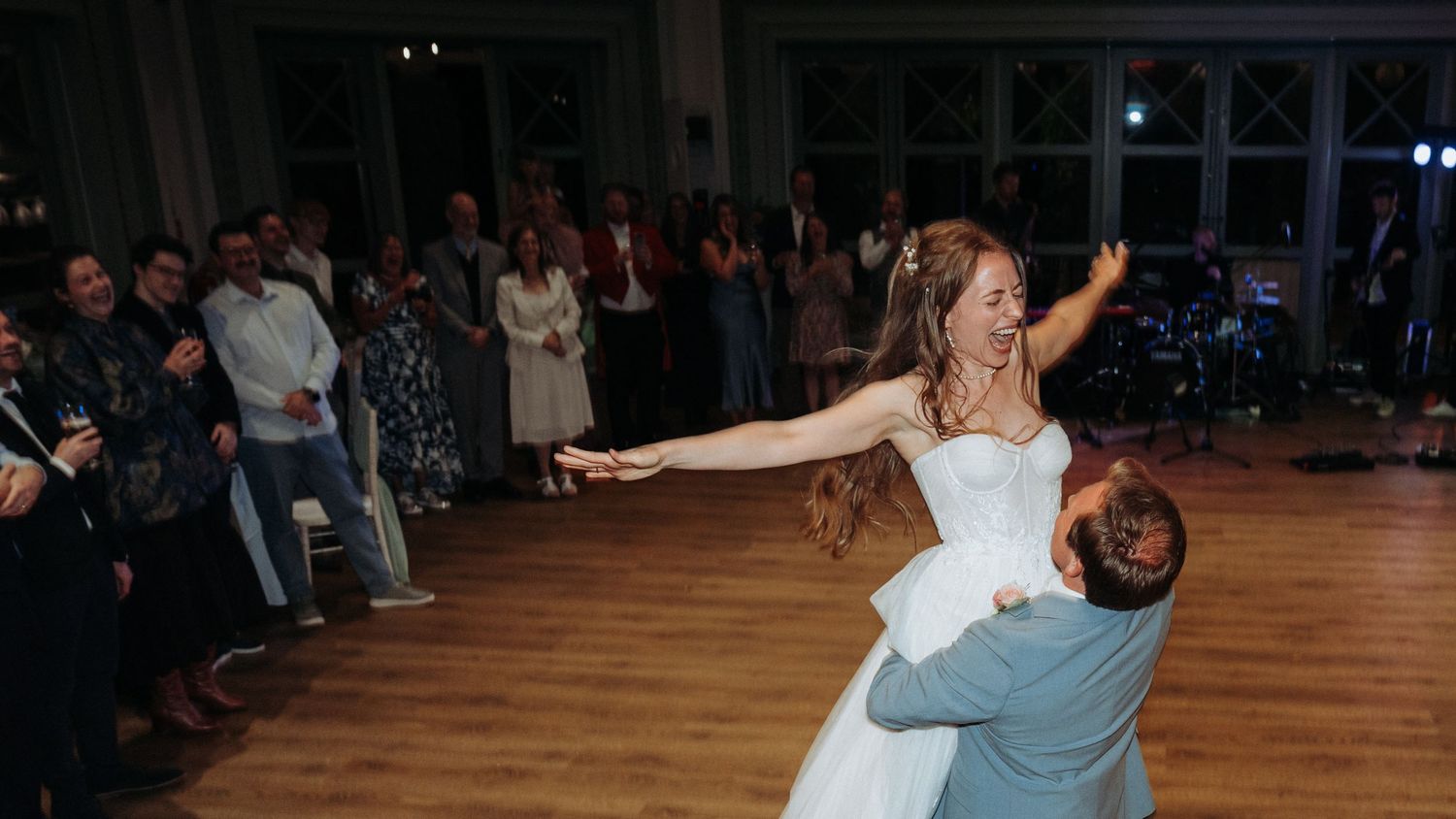 Groom lifting and spinning bride in white ballgown during joyful first dance at wedding.