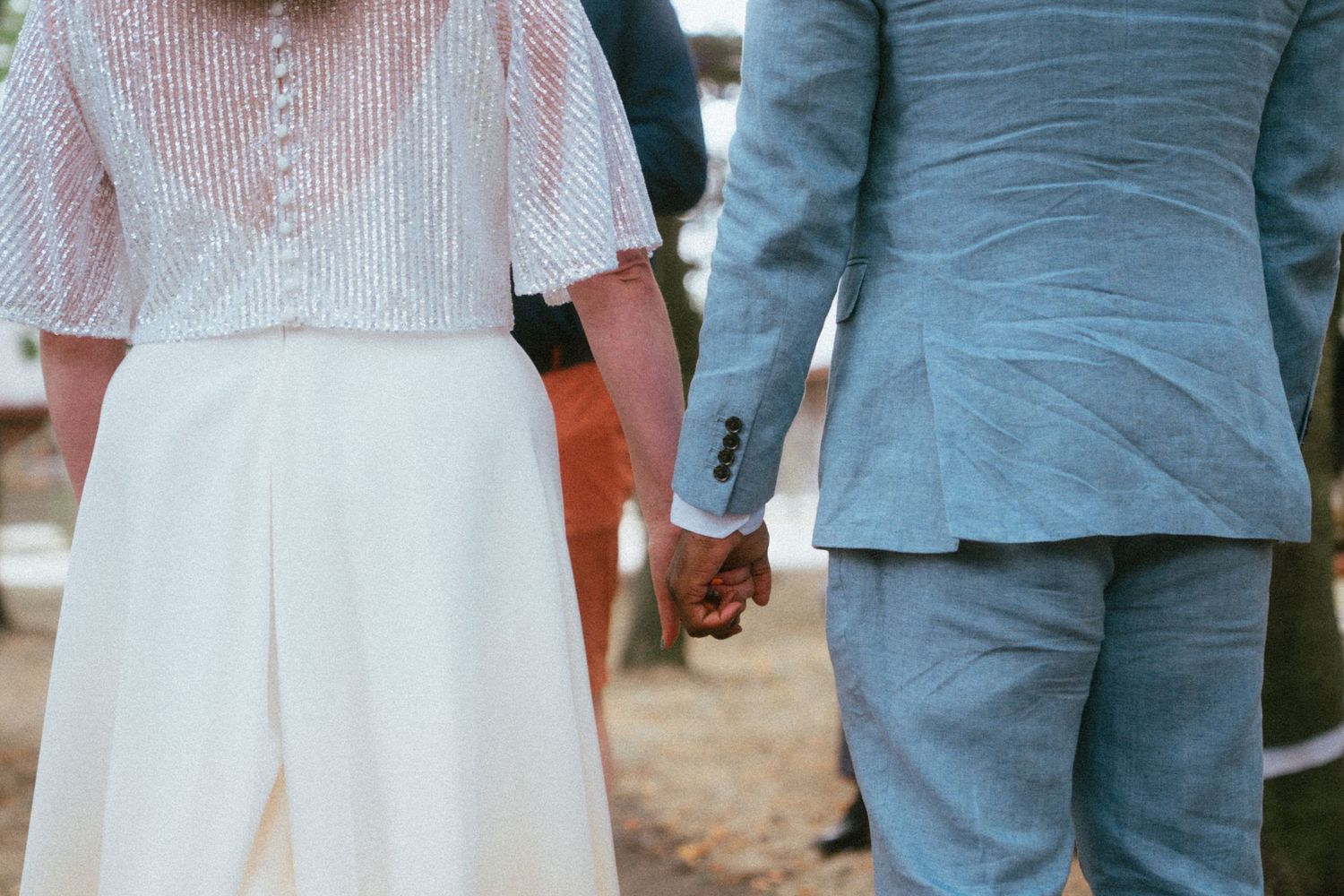 Bride and groom holding hands at outdoor wedding ceremony, bride in white dress, groom in light blue suit.