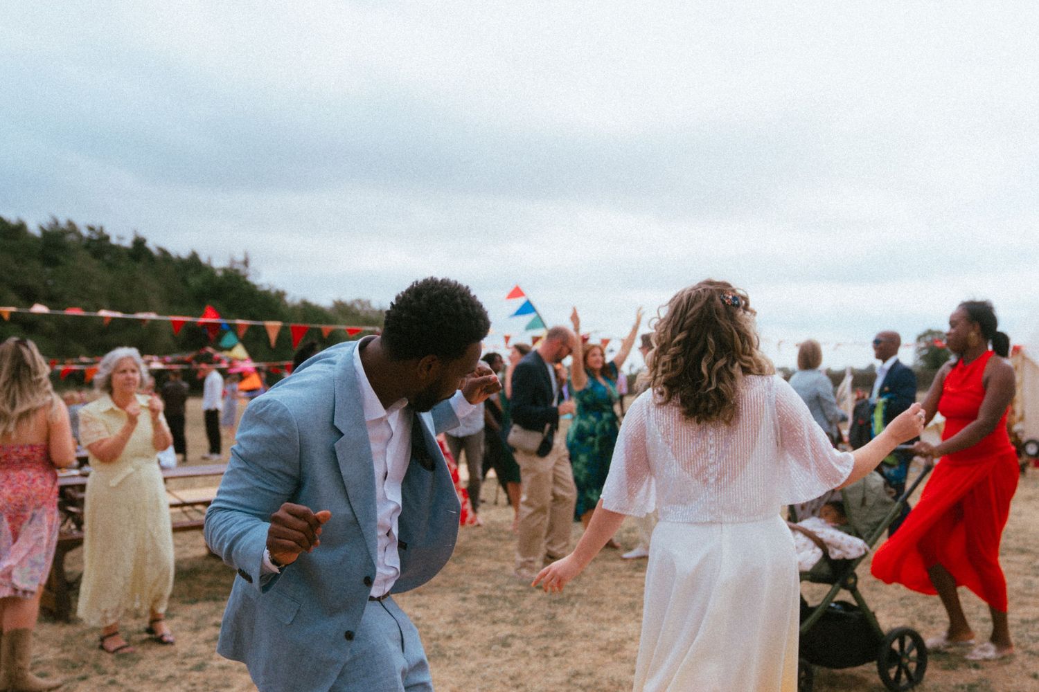 Couple dancing joyfully on a beach wedding celebration with guests and colorful bunting flags in the background.