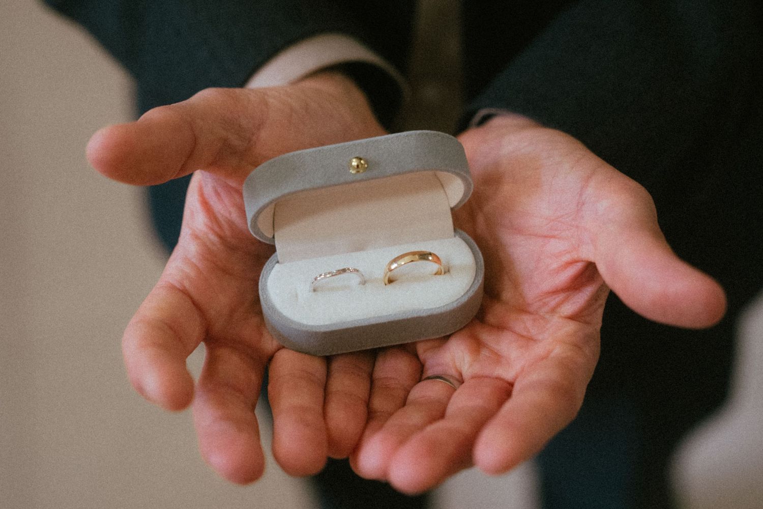 Close-up of hands holding an open ring box with two gold wedding bands inside.