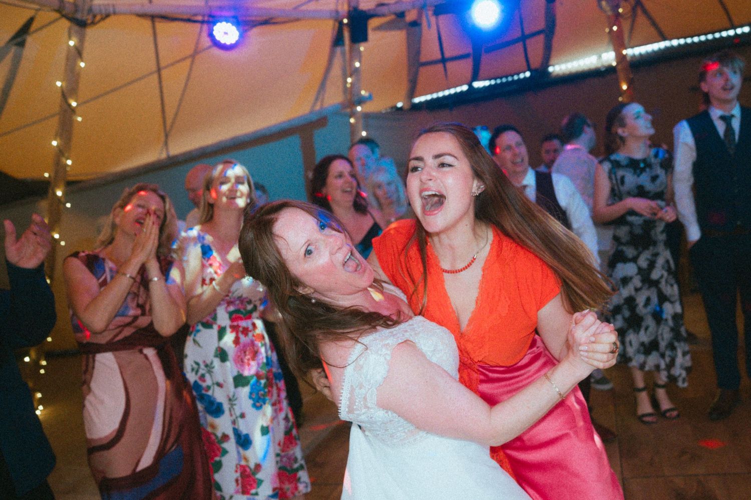 Bride and friend dancing joyfully together at lively wedding reception party.
