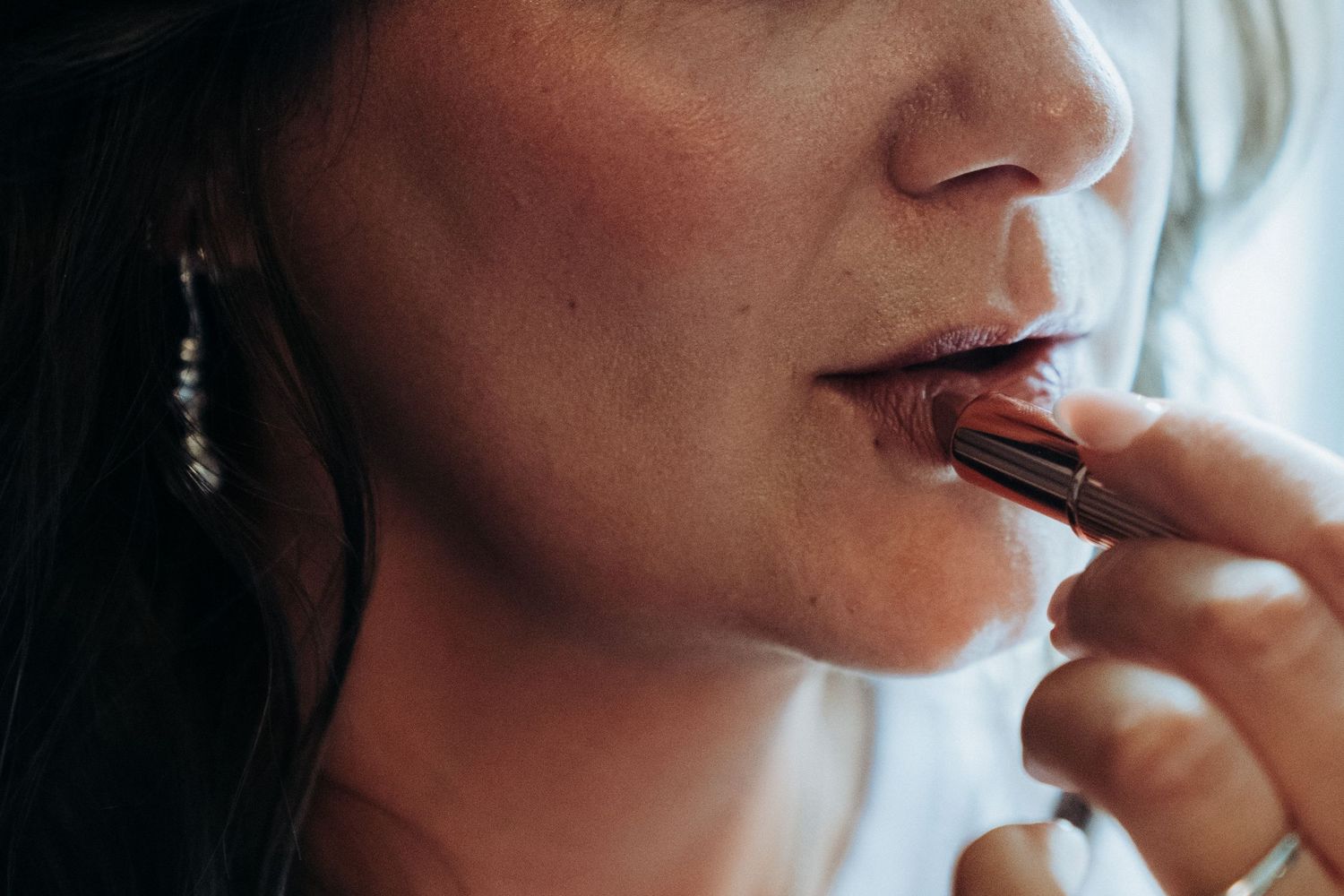 Close-up of a bride applying dark red lipstick with a brush during wedding preparations.