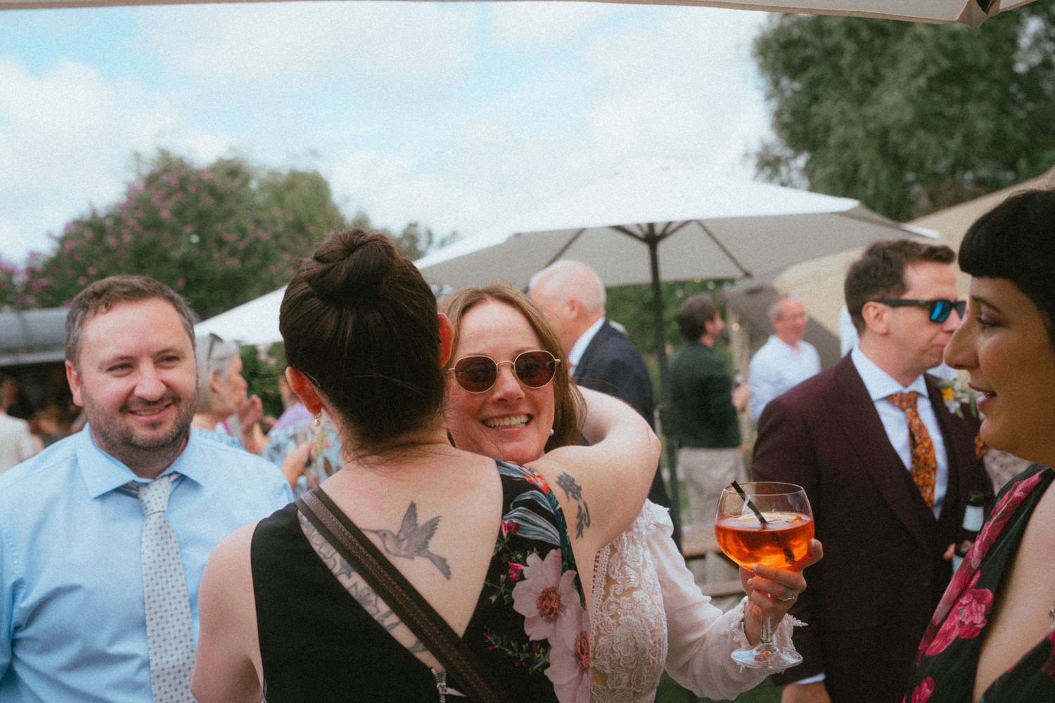 Wedding guests socializing outdoors under white umbrellas, smiling woman holding an aperol spritz.