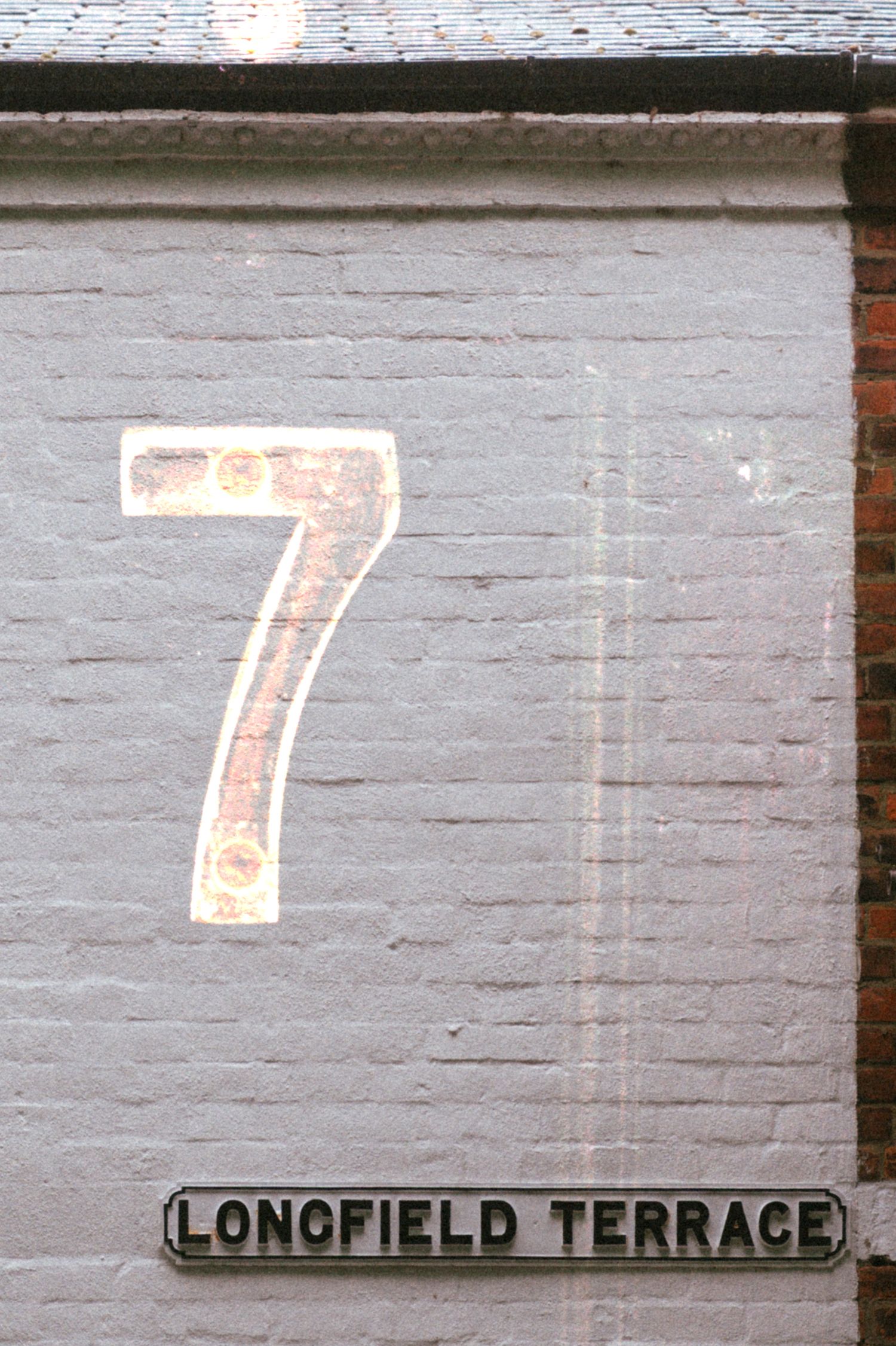 Number 7 painted on a white brick wall above a Longfield Terrace street sign in the UK.