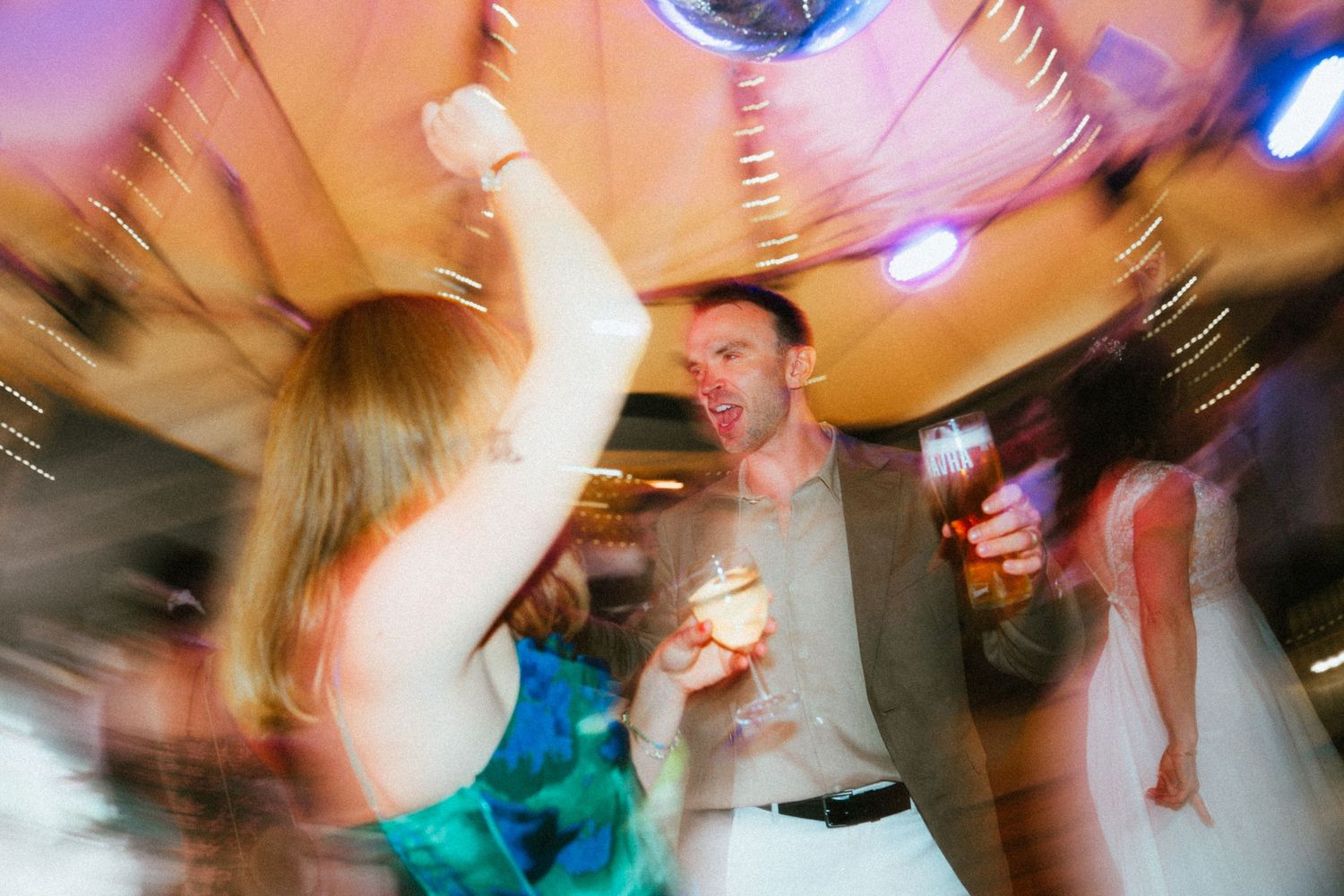 Wedding guests dance energetically under warm lights with motion blur capturing the celebration.