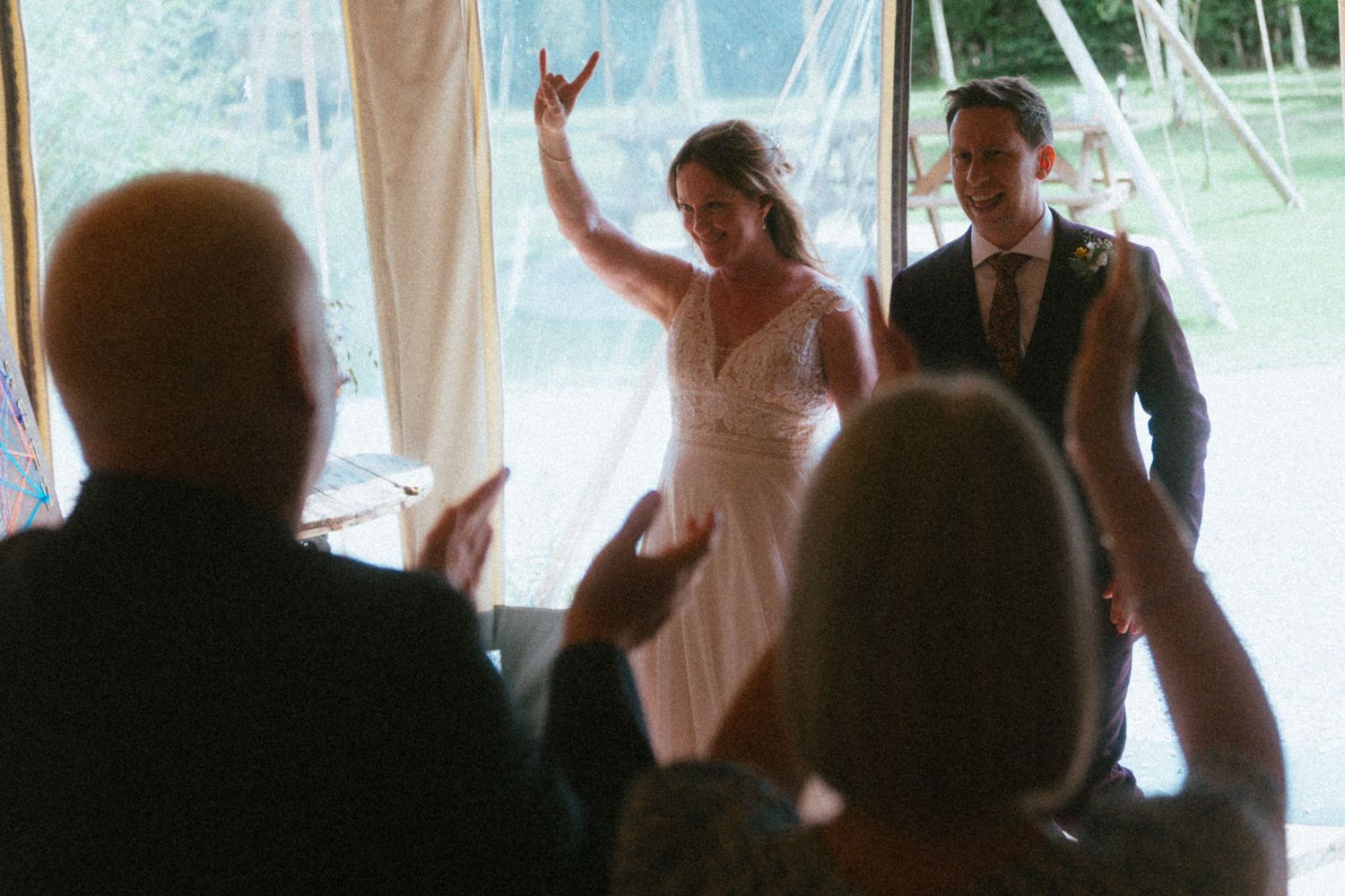 Bride raises hand triumphantly as couple enters wedding reception greeted by cheering guests.