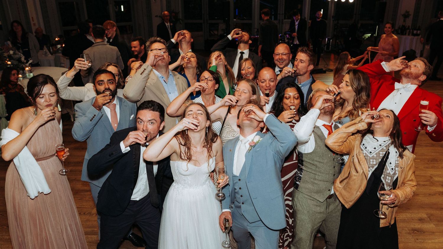Wedding guests and couple joyfully taking shots together on the dance floor at reception.