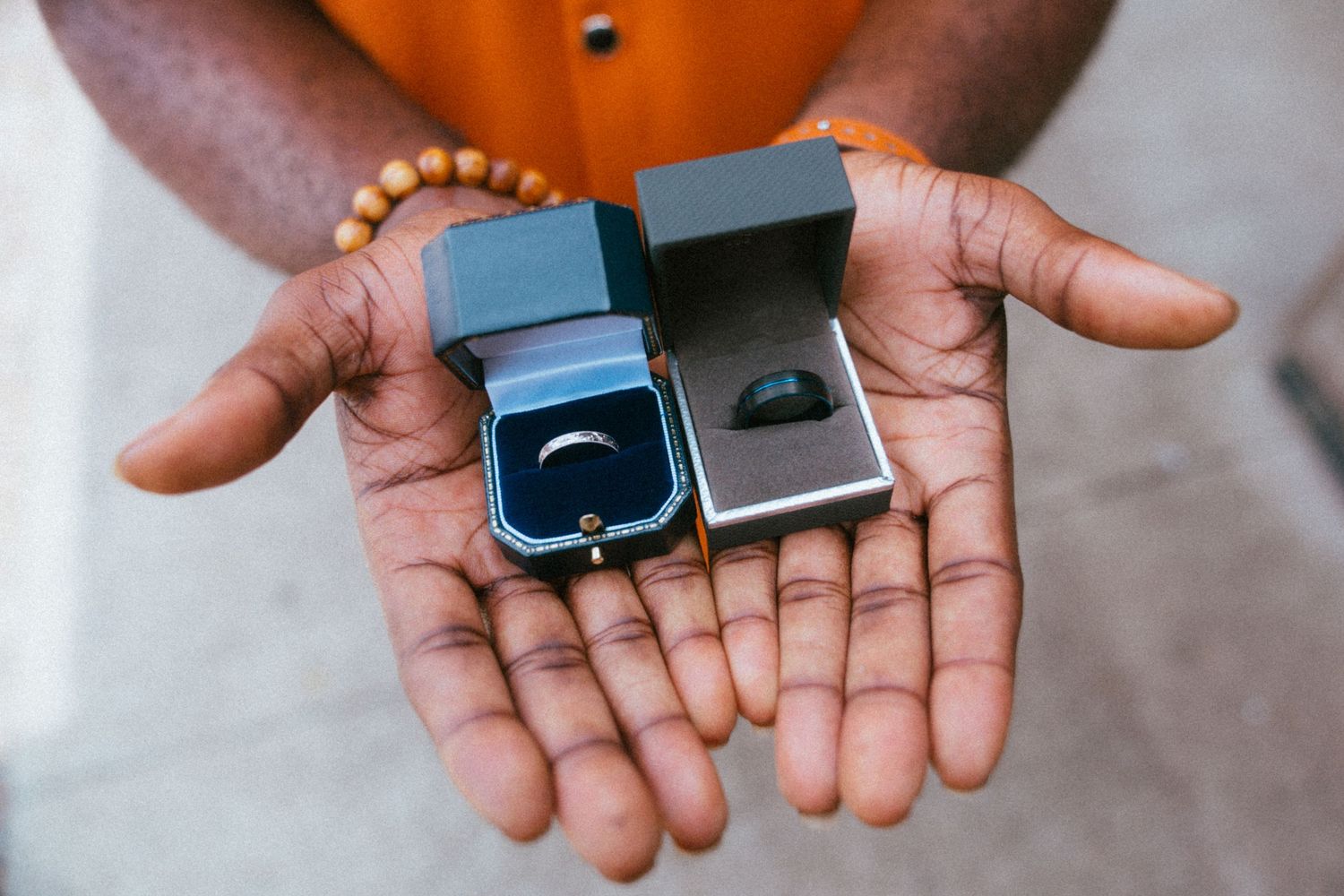 Person holding two open ring boxes with wedding bands in their palms outdoors.