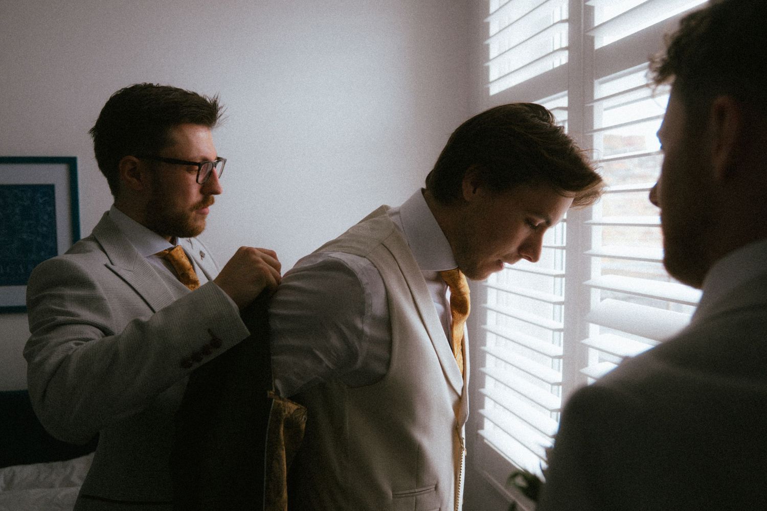 Groomsmen helping groom adjust his suit jacket before wedding ceremony indoors.