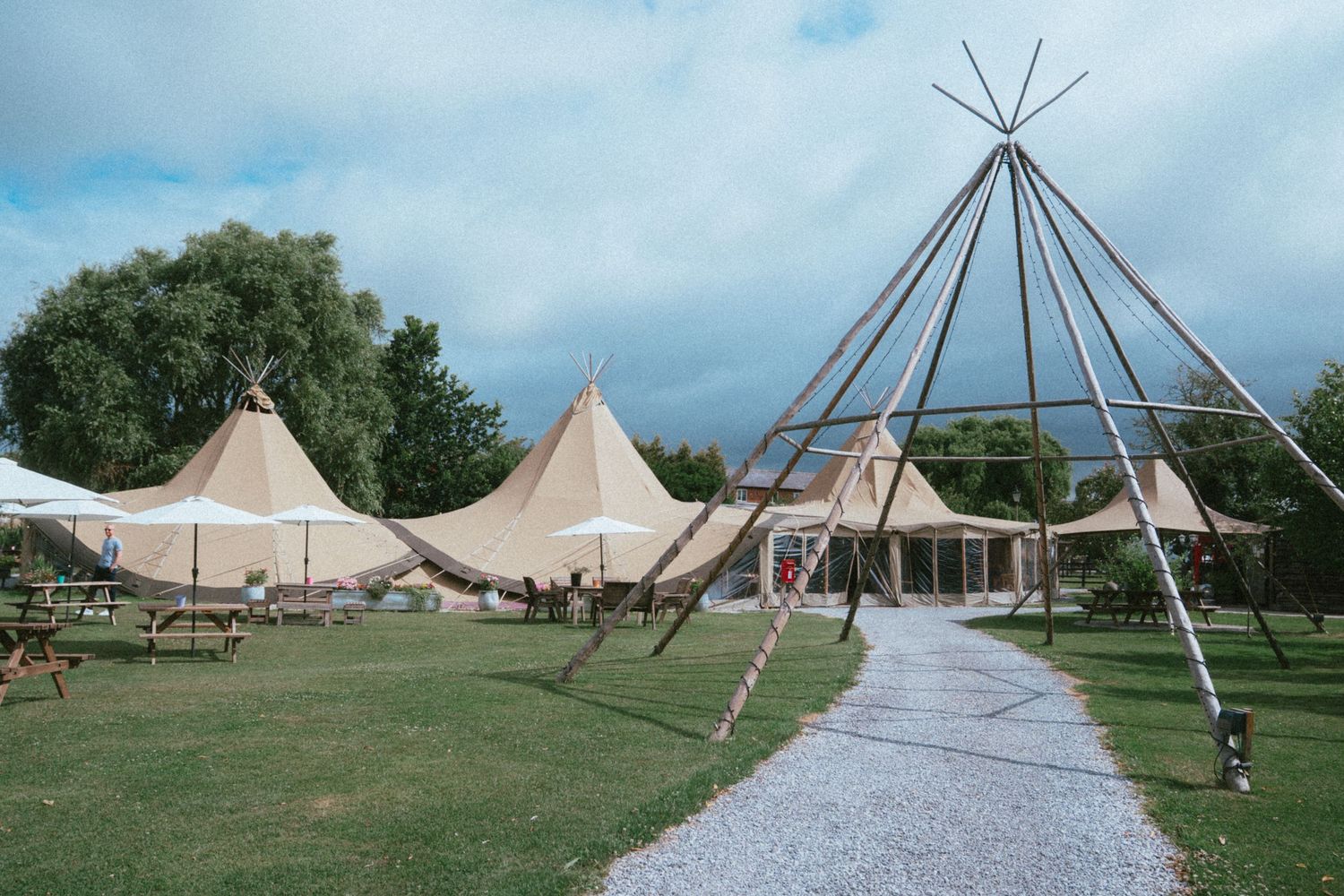 Scenic outdoor wedding venue with tall Nordic tipi tents on lush green lawn under cloudy sky.
