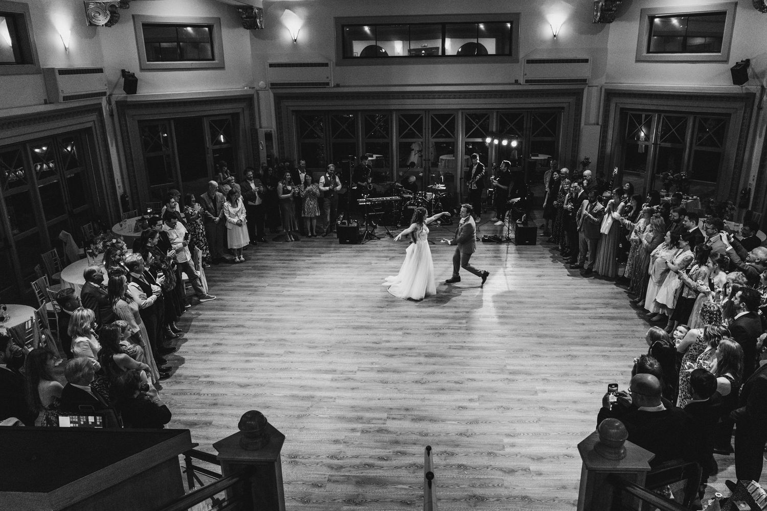 Black and white aerial view of bride and groom sharing first dance surrounded by wedding guests.